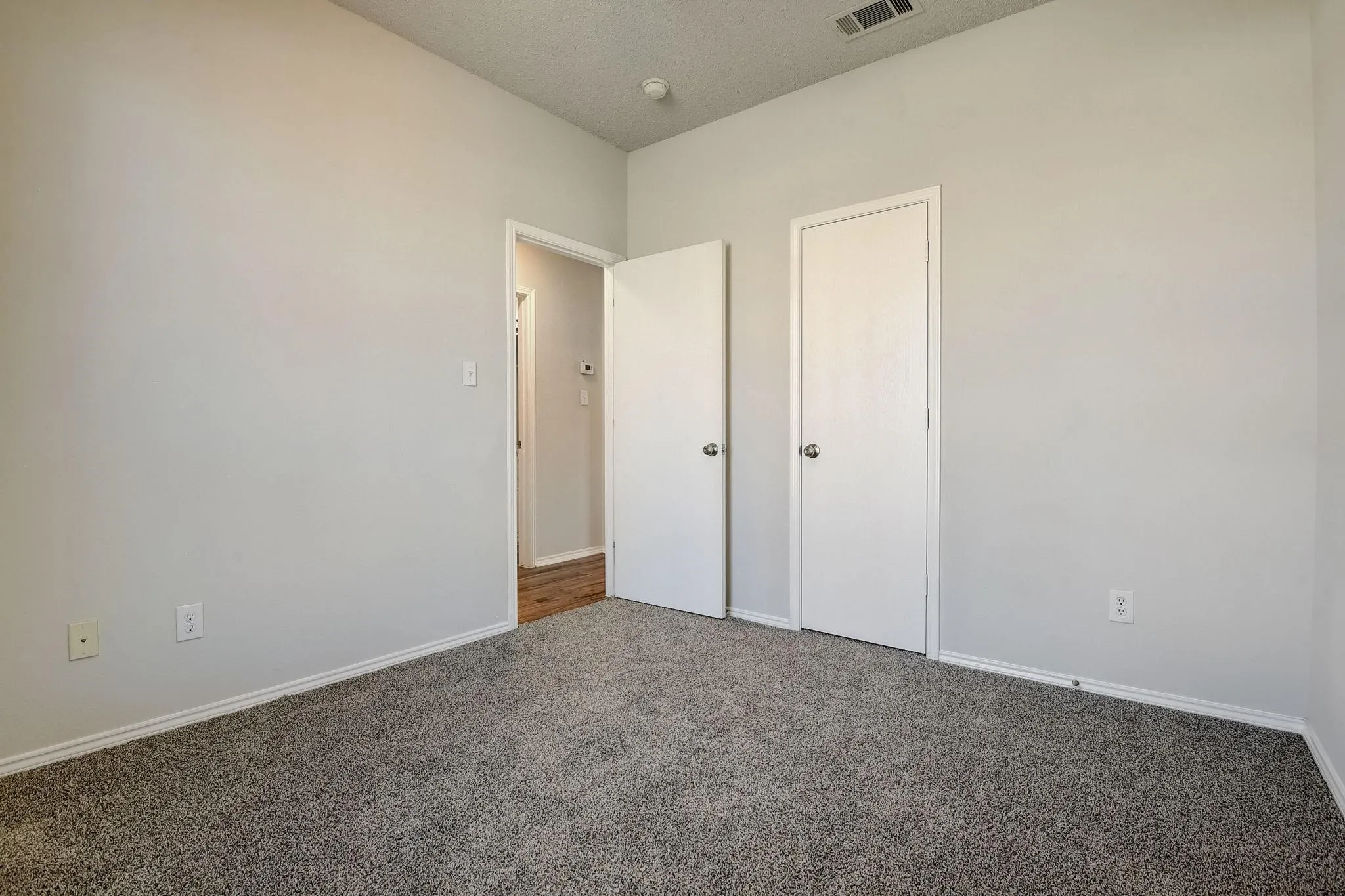 Unfurnished bedroom featuring a textured ceiling, dark colored carpet, visible vents, and baseboards
