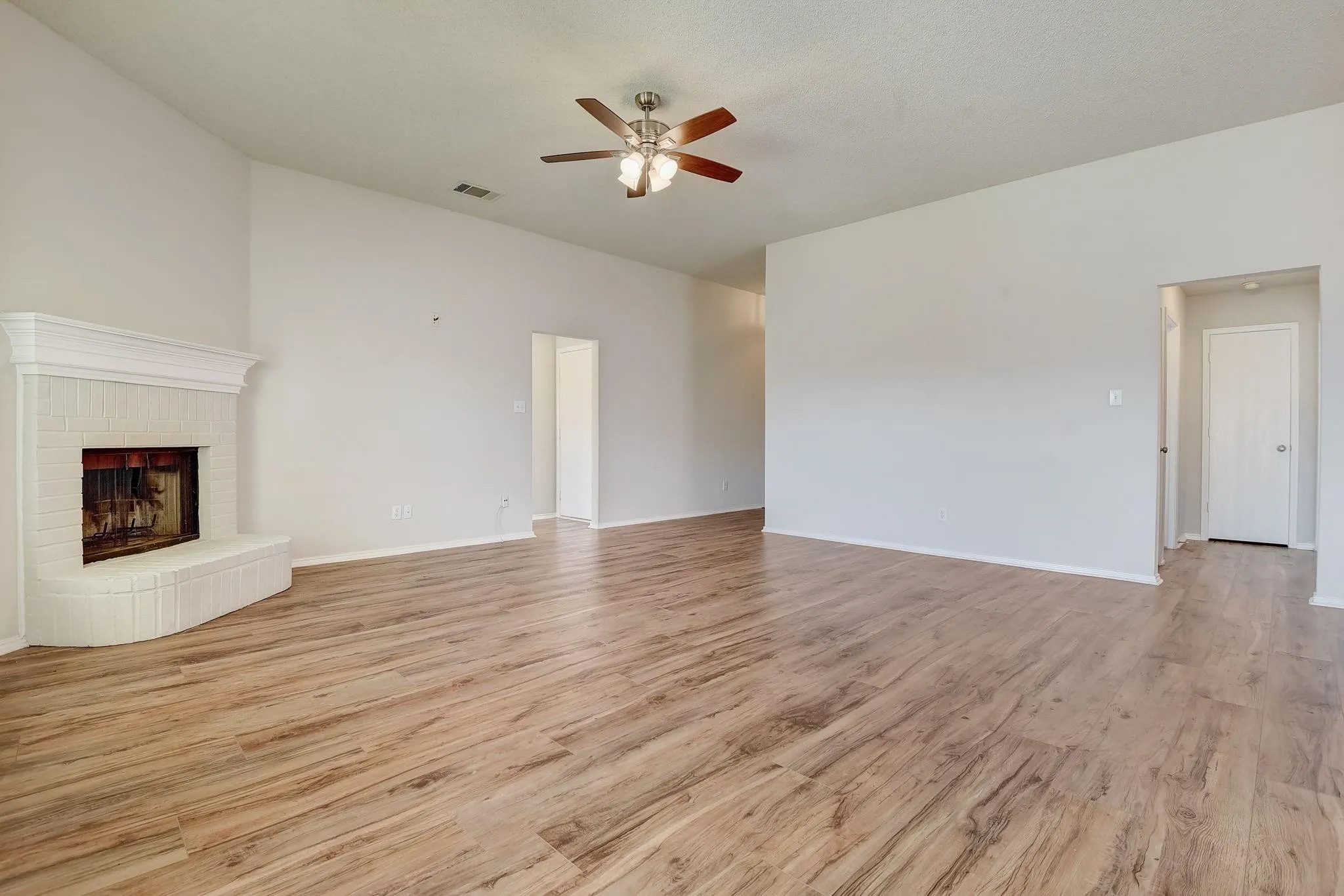 Unfurnished living room with a fireplace, visible vents, ceiling fan, light wood-type flooring, and baseboards