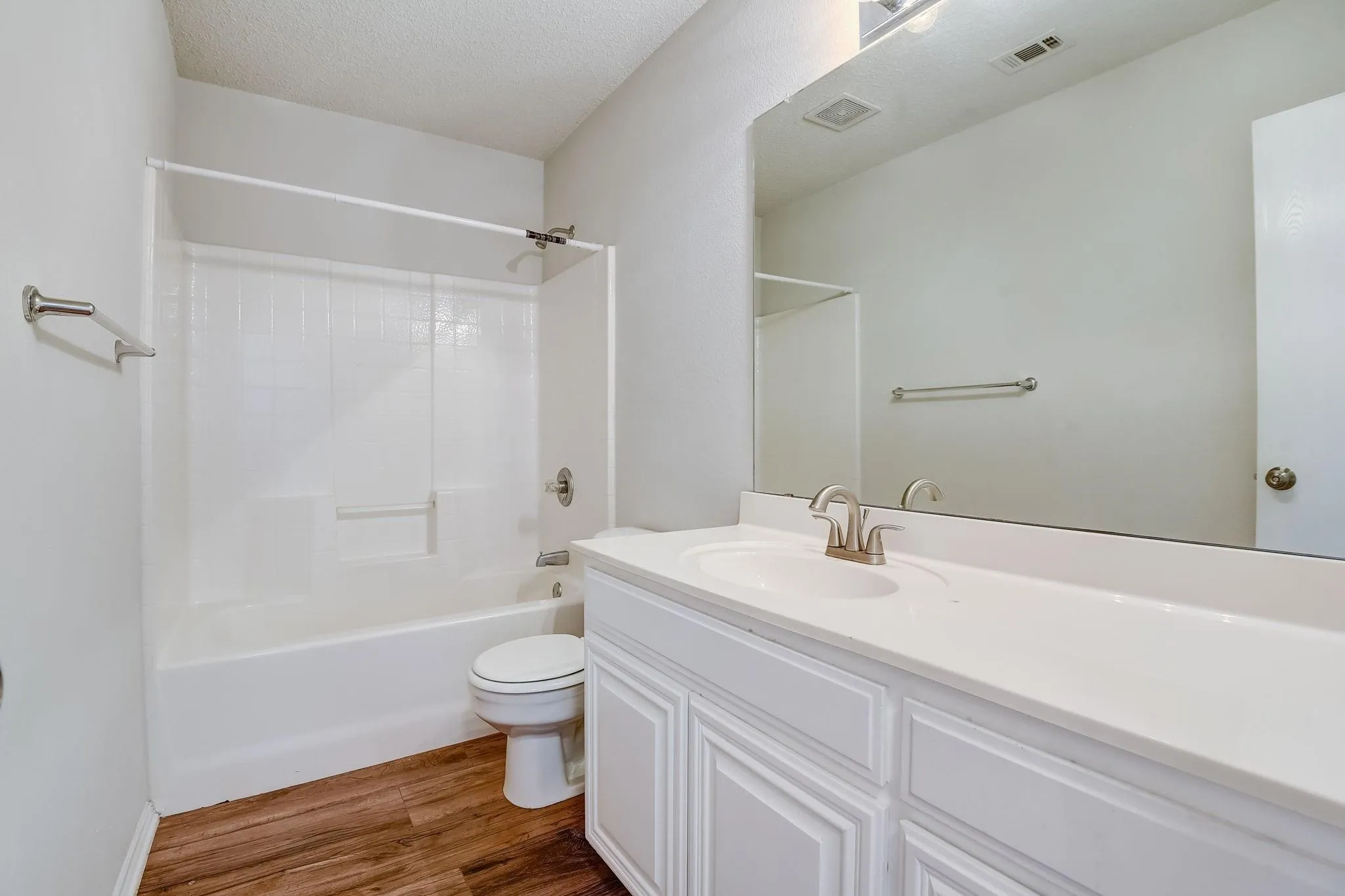 Full bath with a textured ceiling, toilet, wood finished floors, visible vents, and shower / bathing tub combination