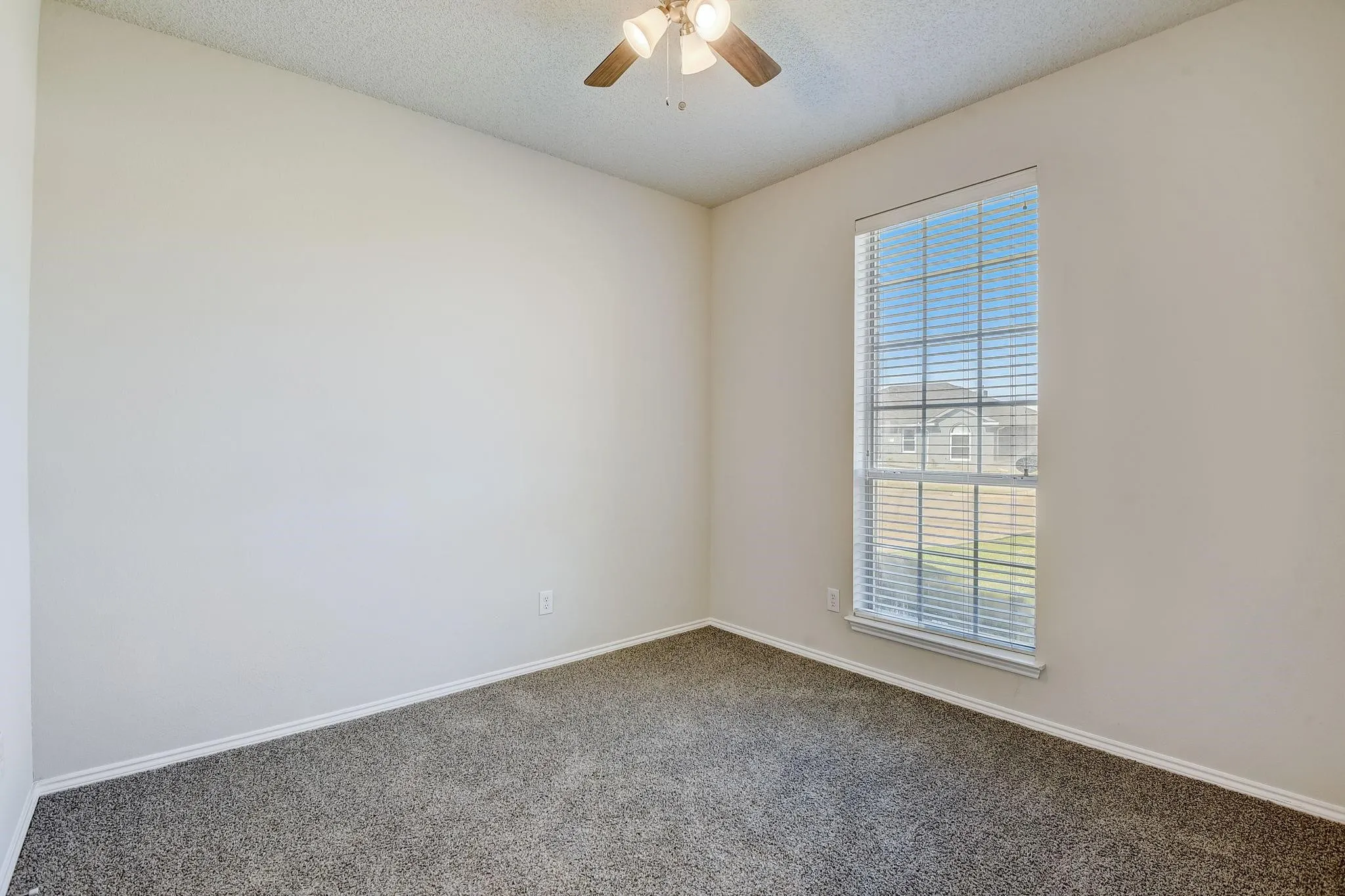 Carpeted spare room with a ceiling fan, a textured ceiling, and baseboards