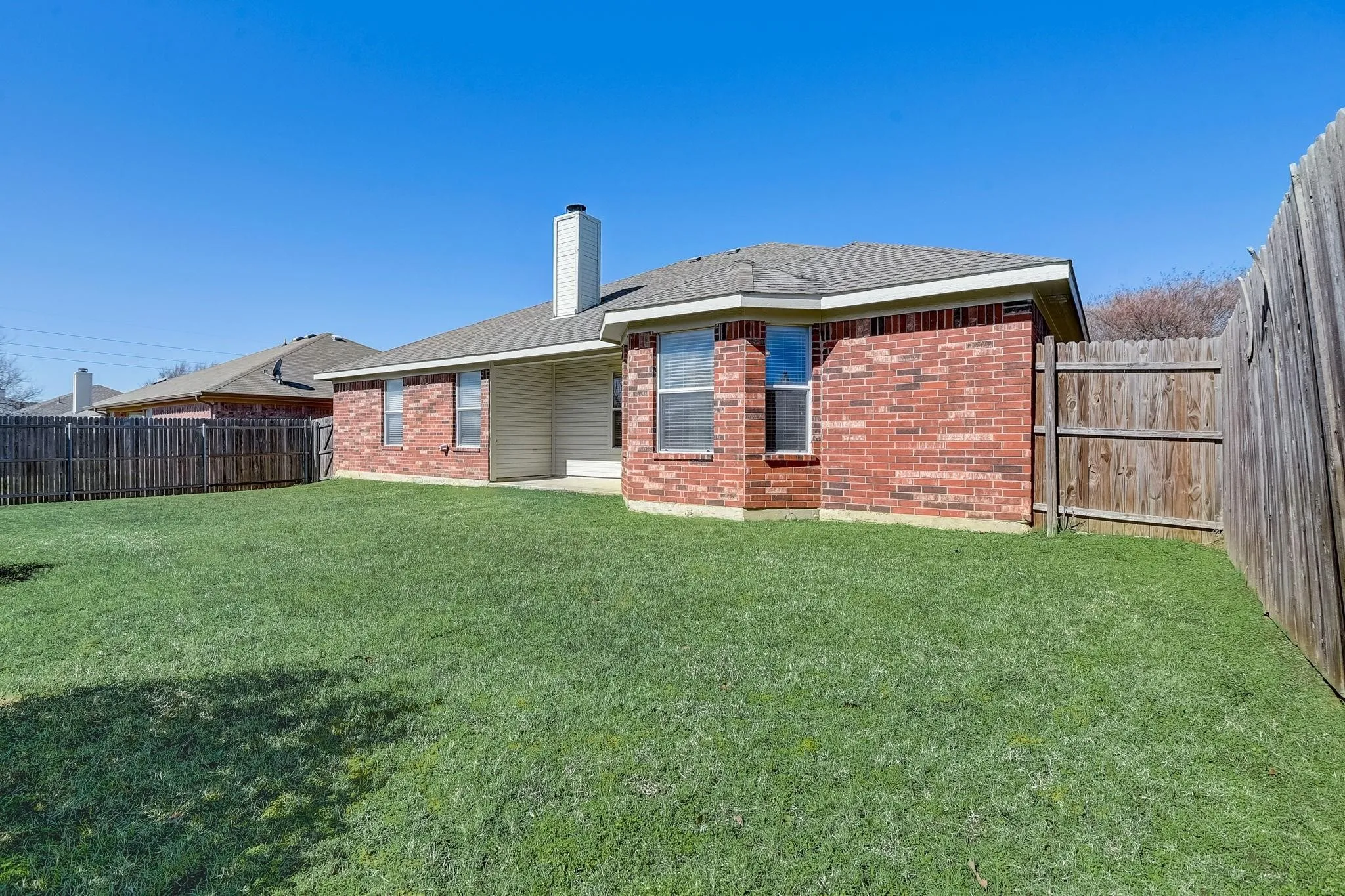Rear view of property featuring brick siding, a lawn, and a fenced backyard