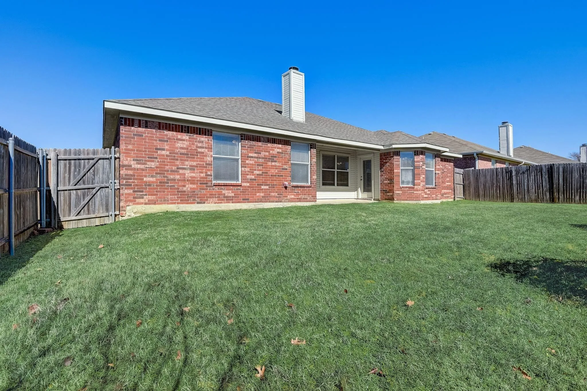 Back of house with a yard, brick siding, and fence