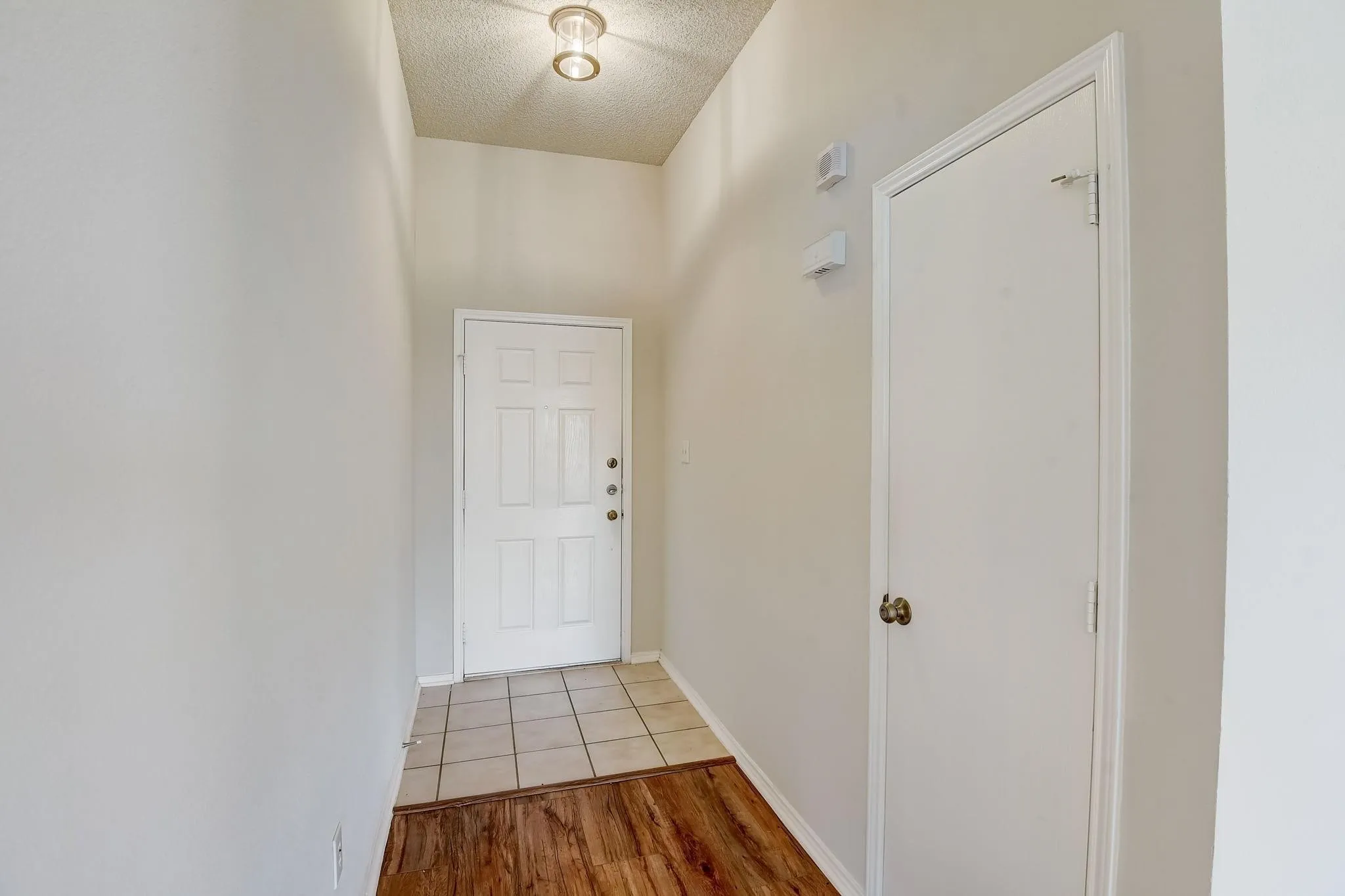 Doorway with light wood-style flooring, baseboards, and a textured ceiling