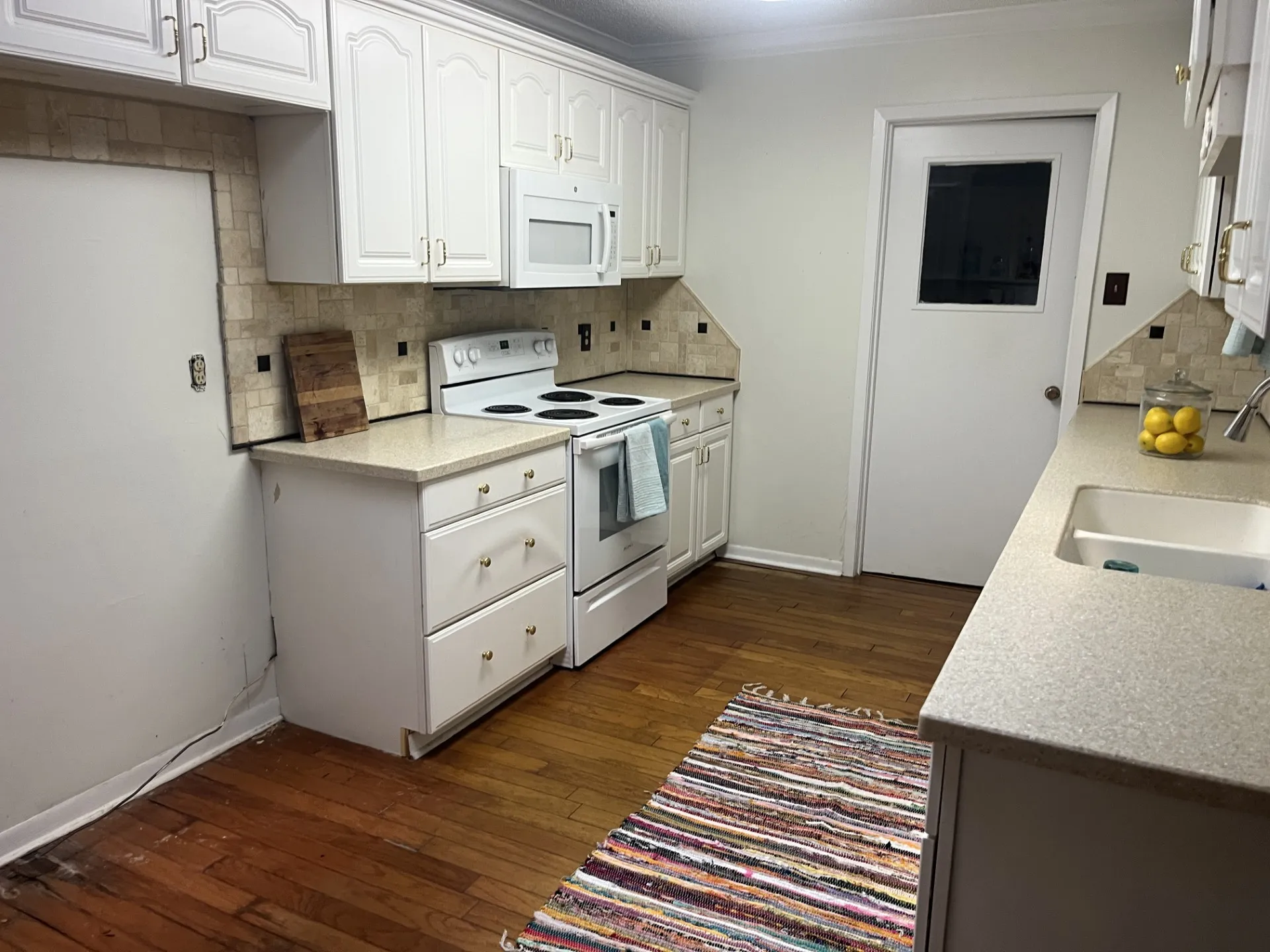 White cabinetry with gold-tone hardware, light-toned countertops, and mosaic tile backsplash