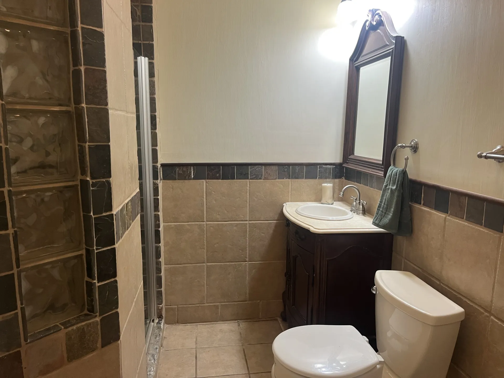 Tiled shower with glass block accent, wood-finish vanity with countertop sink, framed mirror, and wall-mounted lighting