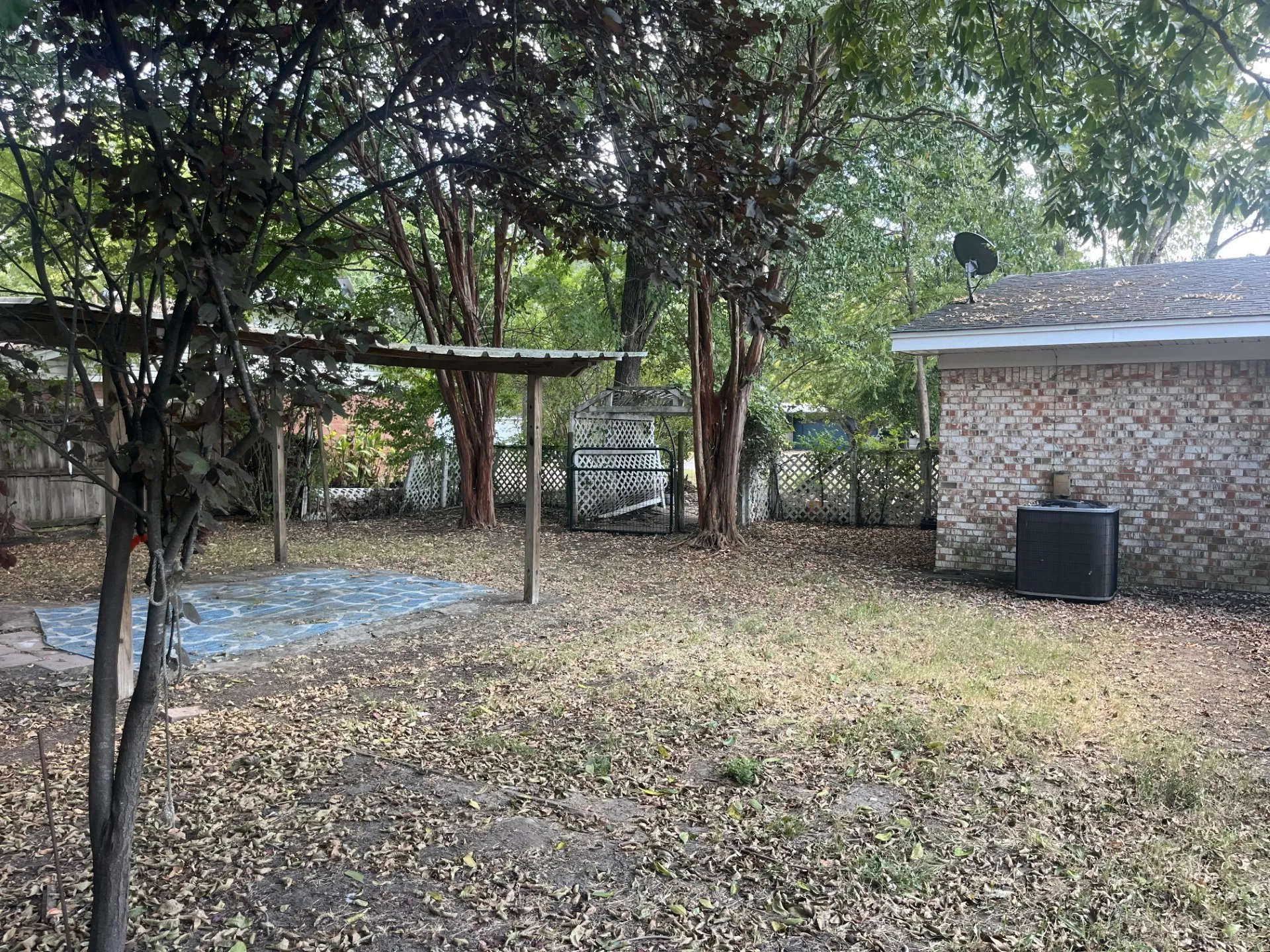Expansive yard featuring mature trees, a covered patio structure, and a brick exterior building