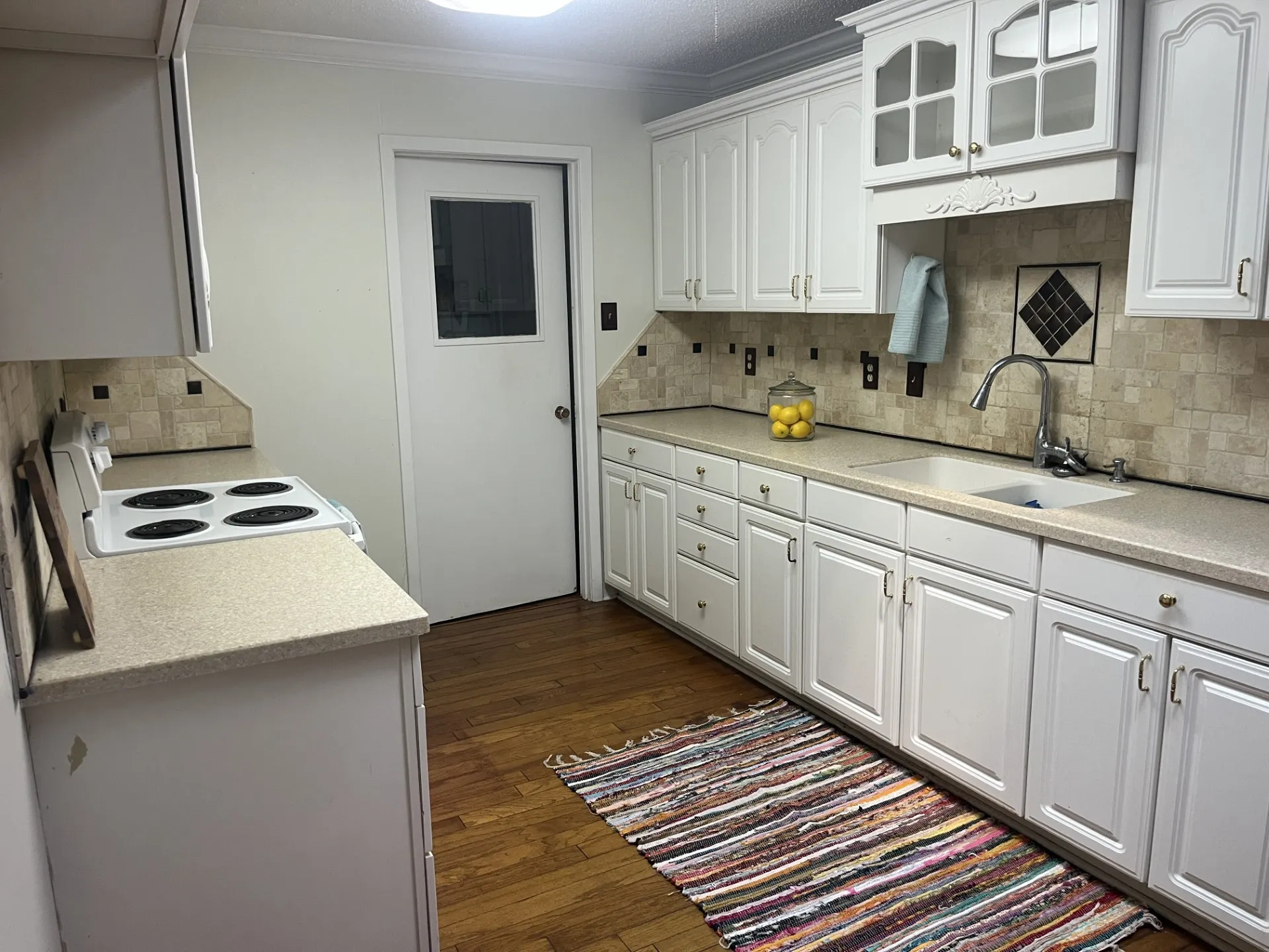 White cabinetry with glass-front uppers, tile backsplash, and light-toned countertops