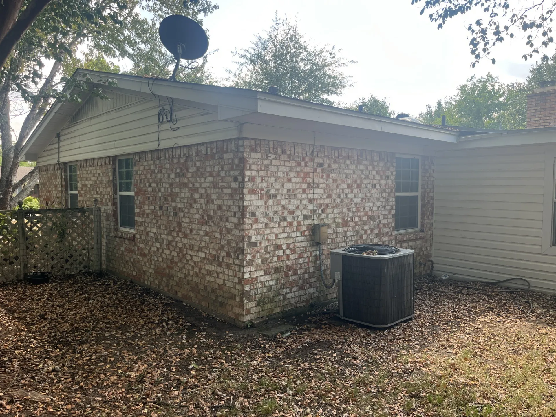 Brick and siding exterior with multiple windows, a lattice fence, and central air conditioning unit