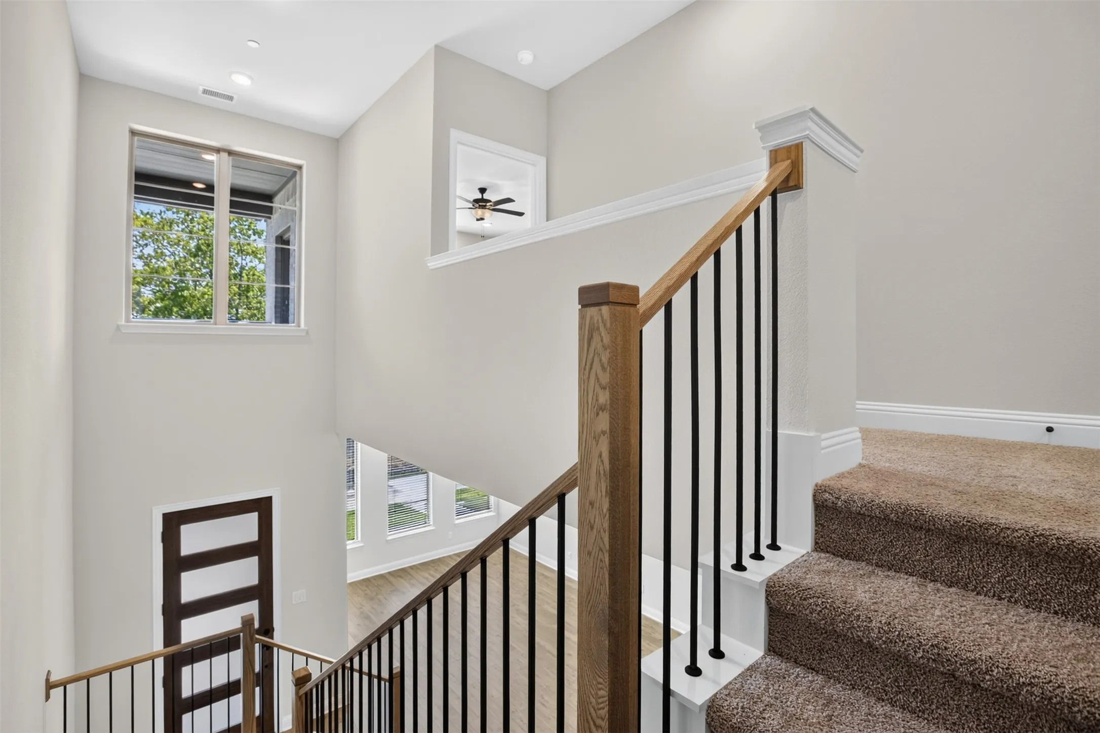 Two-story foyer with large windows, wood-finish flooring, and a staircase featuring wood newel posts, railings, and black metal balusters