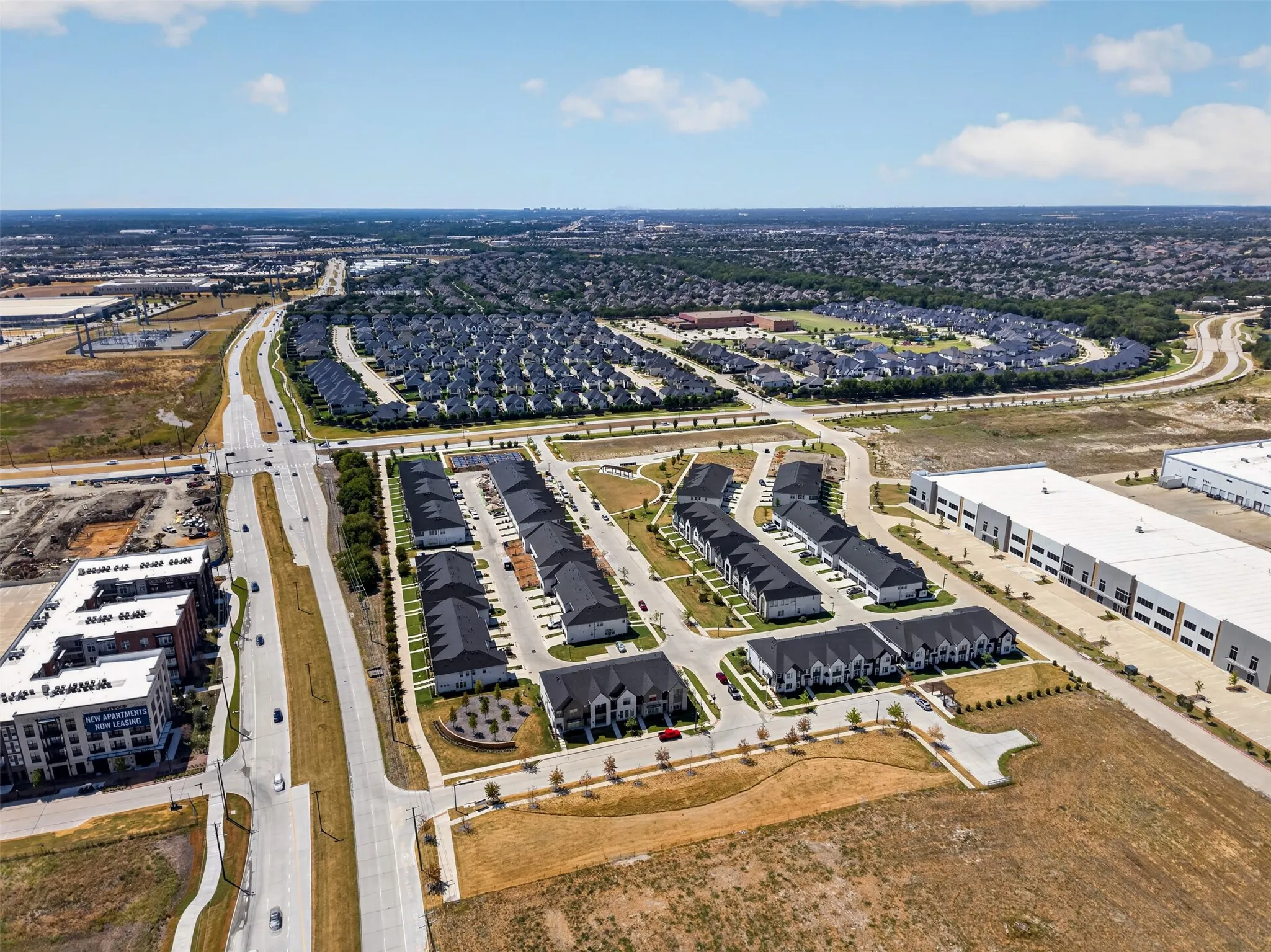 Aerial perspective showcasing a residential development with multiple unit styles, adjacent commercial structures, and a prominent roadway