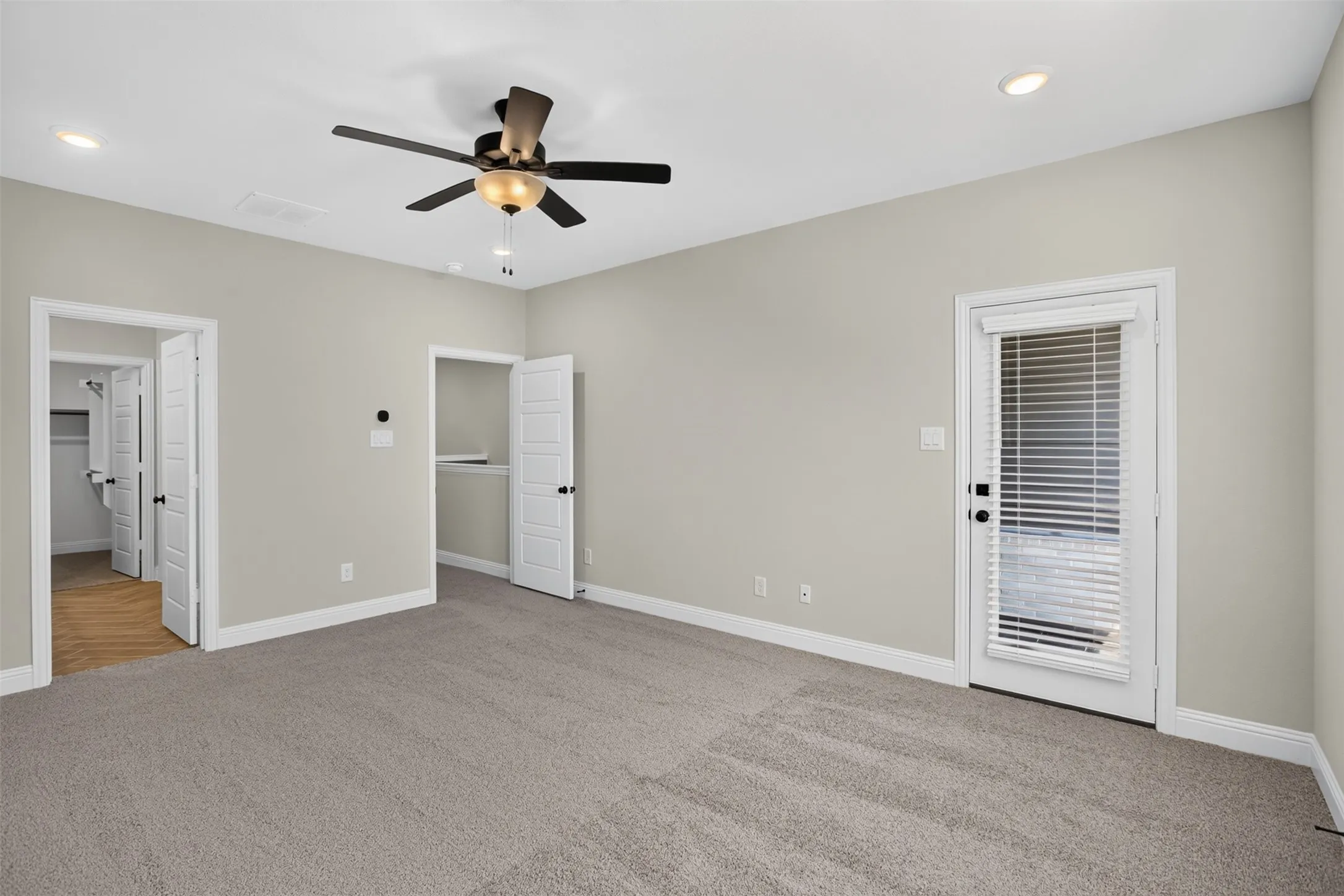 Neutral tone wall paint, carpet flooring, ceiling fan with light fixture, recessed lighting, and a glass-paneled door with blinds