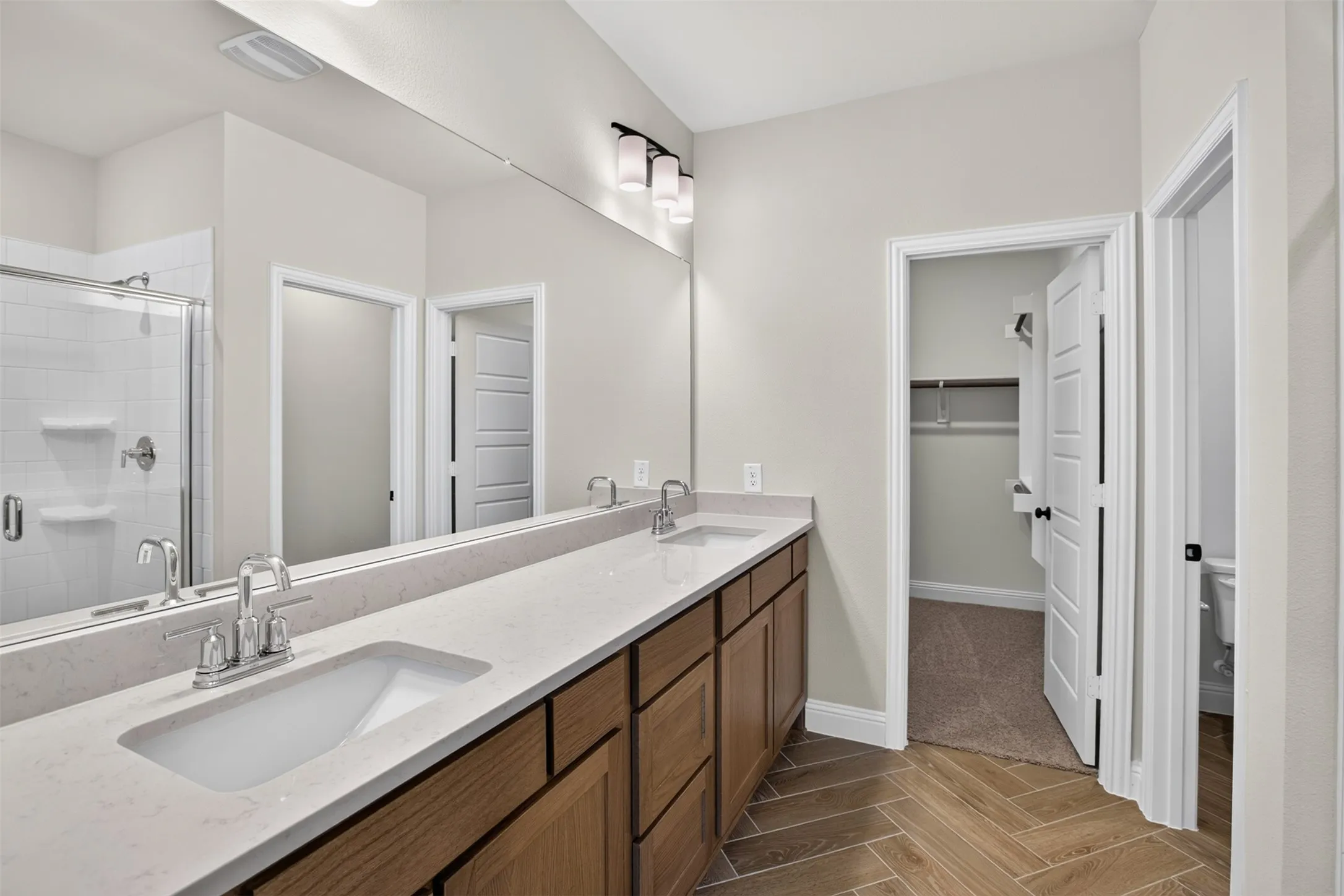 Dual vanity with stone countertop, wood-finish cabinetry, chrome fixtures, and a large wall mirror