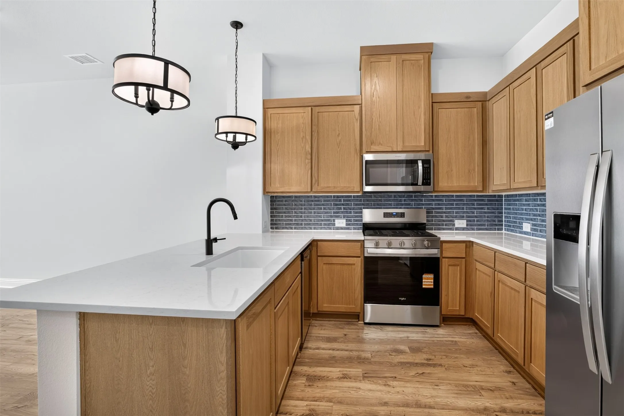 Kitchen featuring wood-finish cabinetry, stainless steel appliances, blue tile backsplash, white countertops, and wood-finish flooring