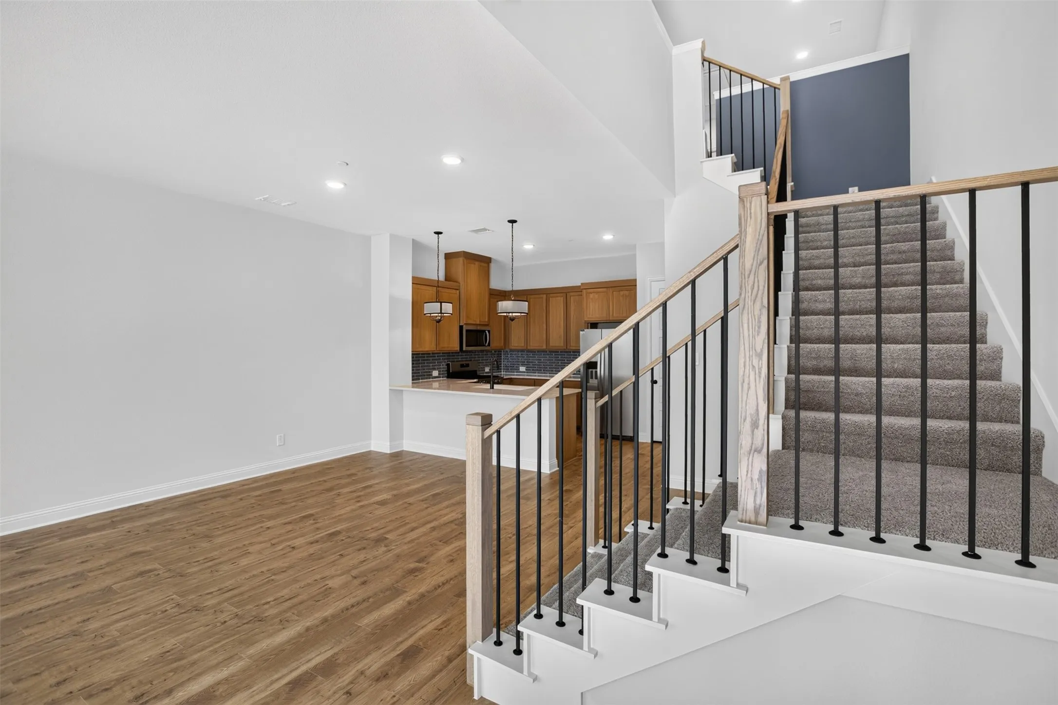 Open-concept living area with wood-finish flooring, recessed lighting, and a modern staircase featuring black metal balusters