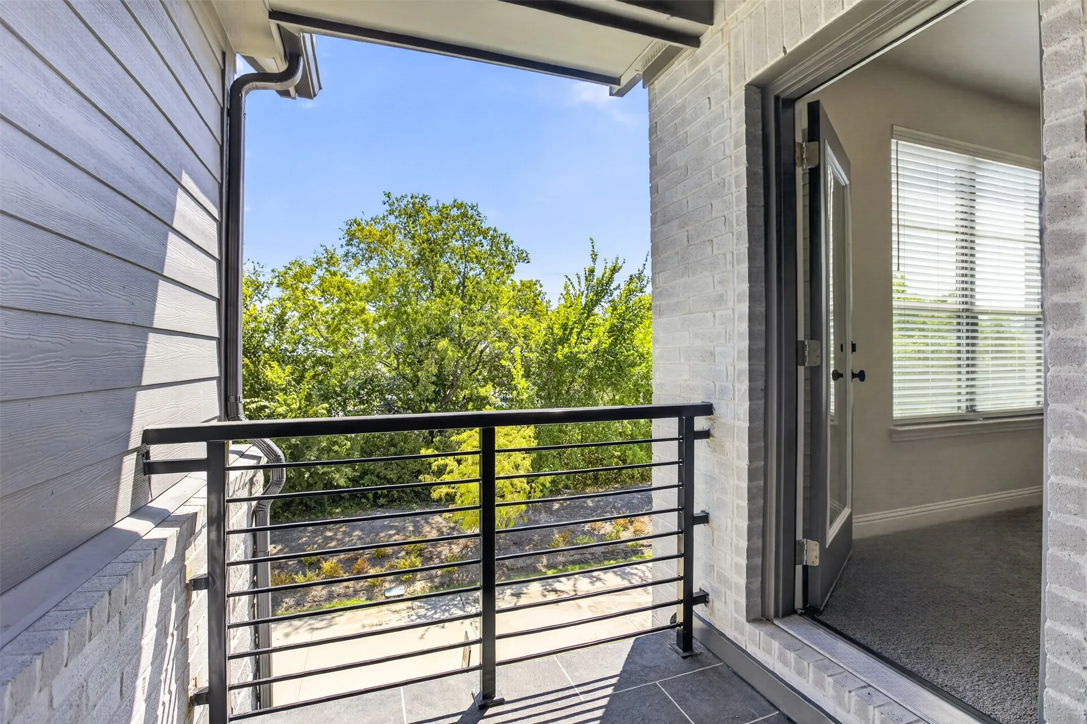 Private balcony featuring dark tile flooring, a horizontal metal railing, and light brick exterior