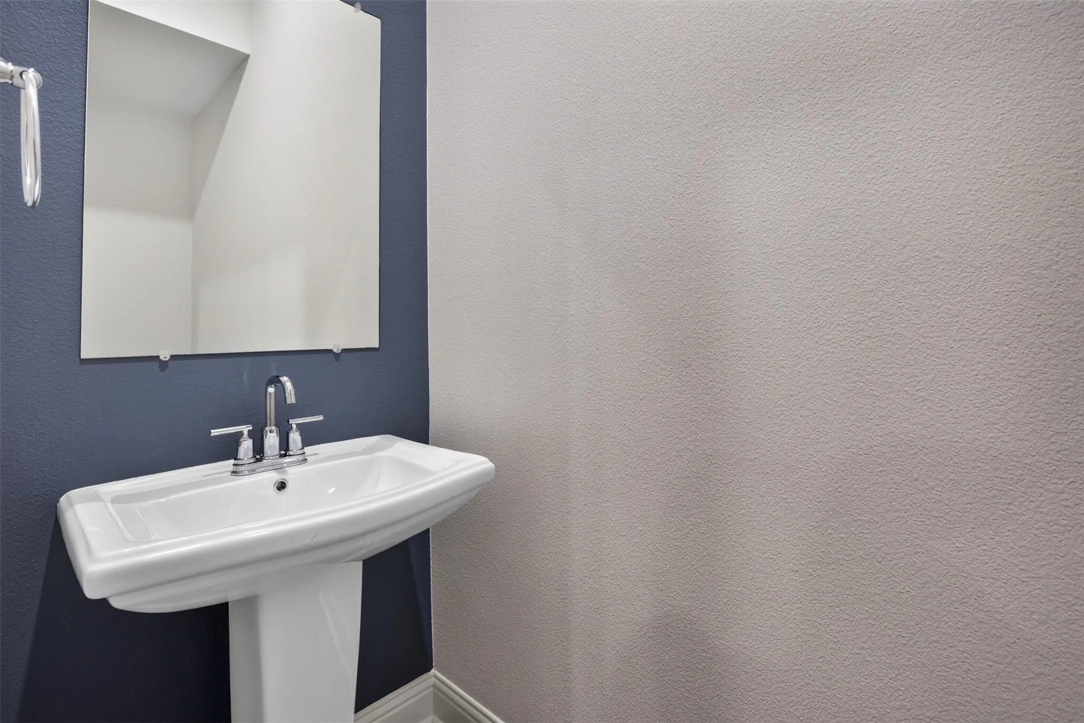 Pedestal sink with chrome fixtures, a frameless wall mirror, and contrasting wall colors