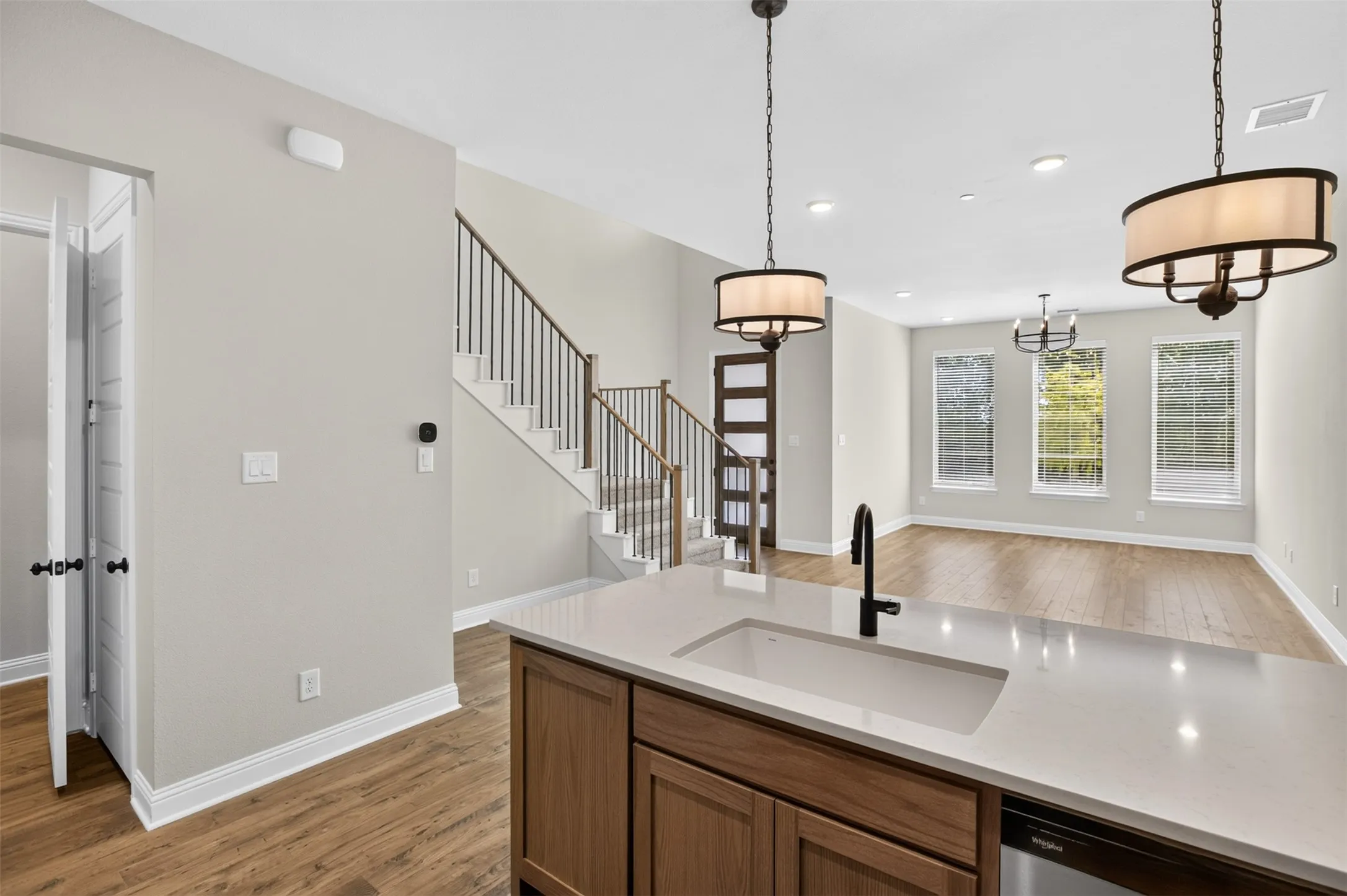 Open-concept living space with wood-finish flooring, a contemporary staircase with metal balusters, and a kitchen island featuring an undermount sink and a matte black faucet