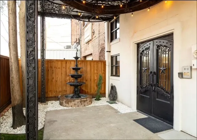 Wrought iron double entry doors with star accents, a multi-tiered fountain feature, and a wood plank privacy fence