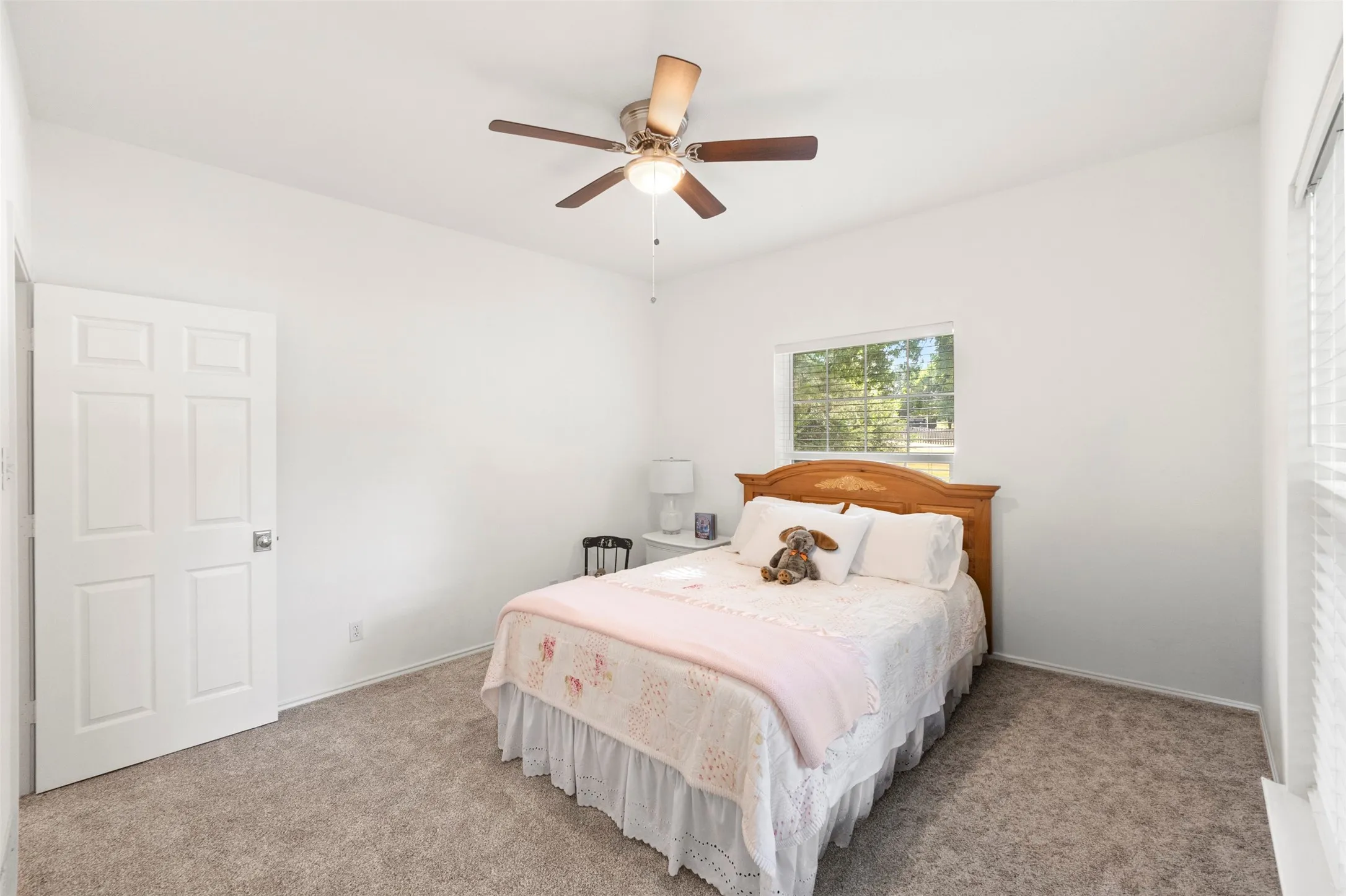 Ceiling fan with wood-finish blades, white paneled door, window with blinds, and carpeted flooring