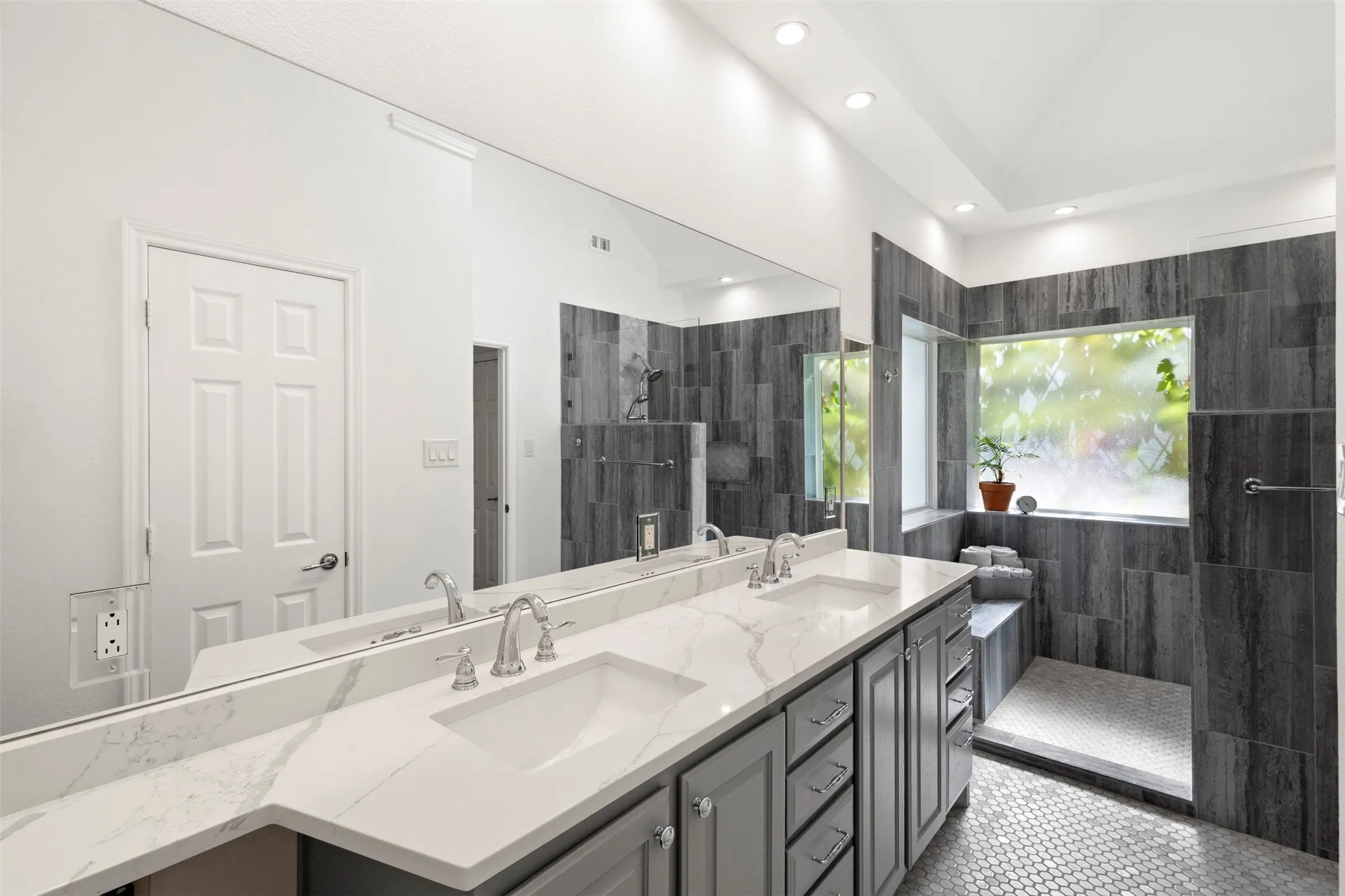 Spa-inspired primary bathroom featuring dual vanities with white quartz countertops, polished chrome fixtures, and abundant mirror lighting