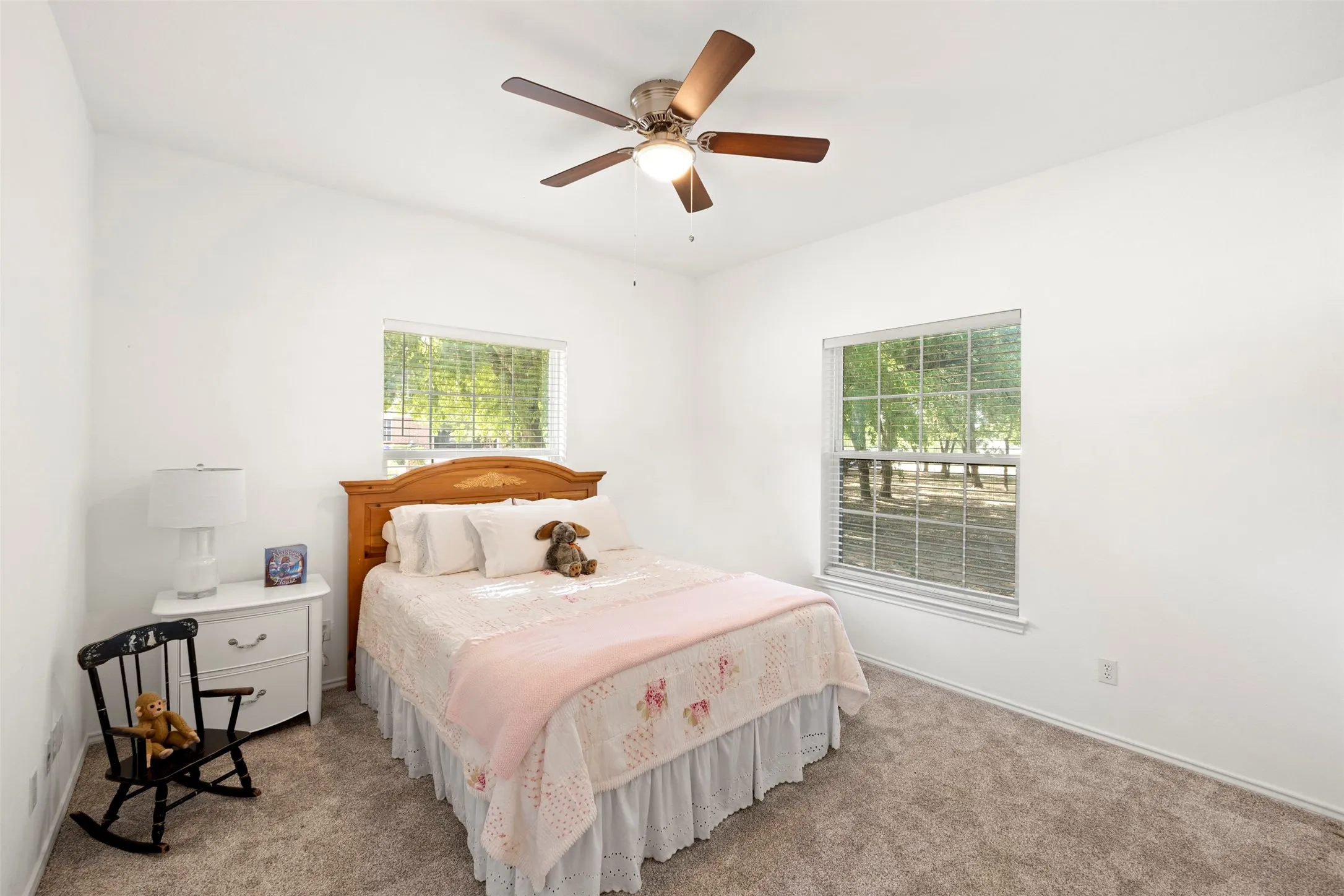 Carpeted flooring, two windows with blinds, ceiling fan with light fixture, and white walls