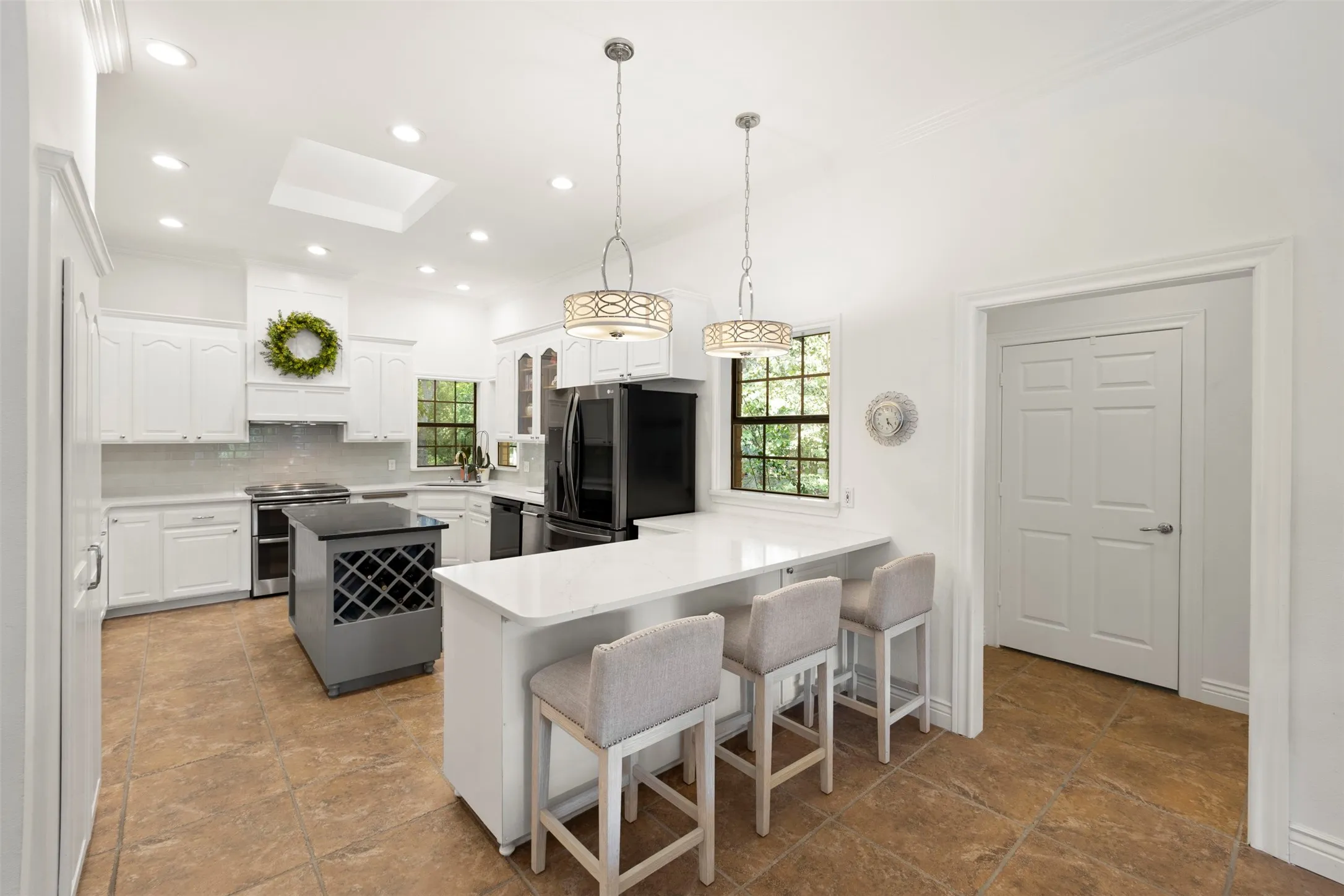 Spacious kitchen featuring white cabinetry, light-toned countertops, a central island with wine storage, and an integrated breakfast bar