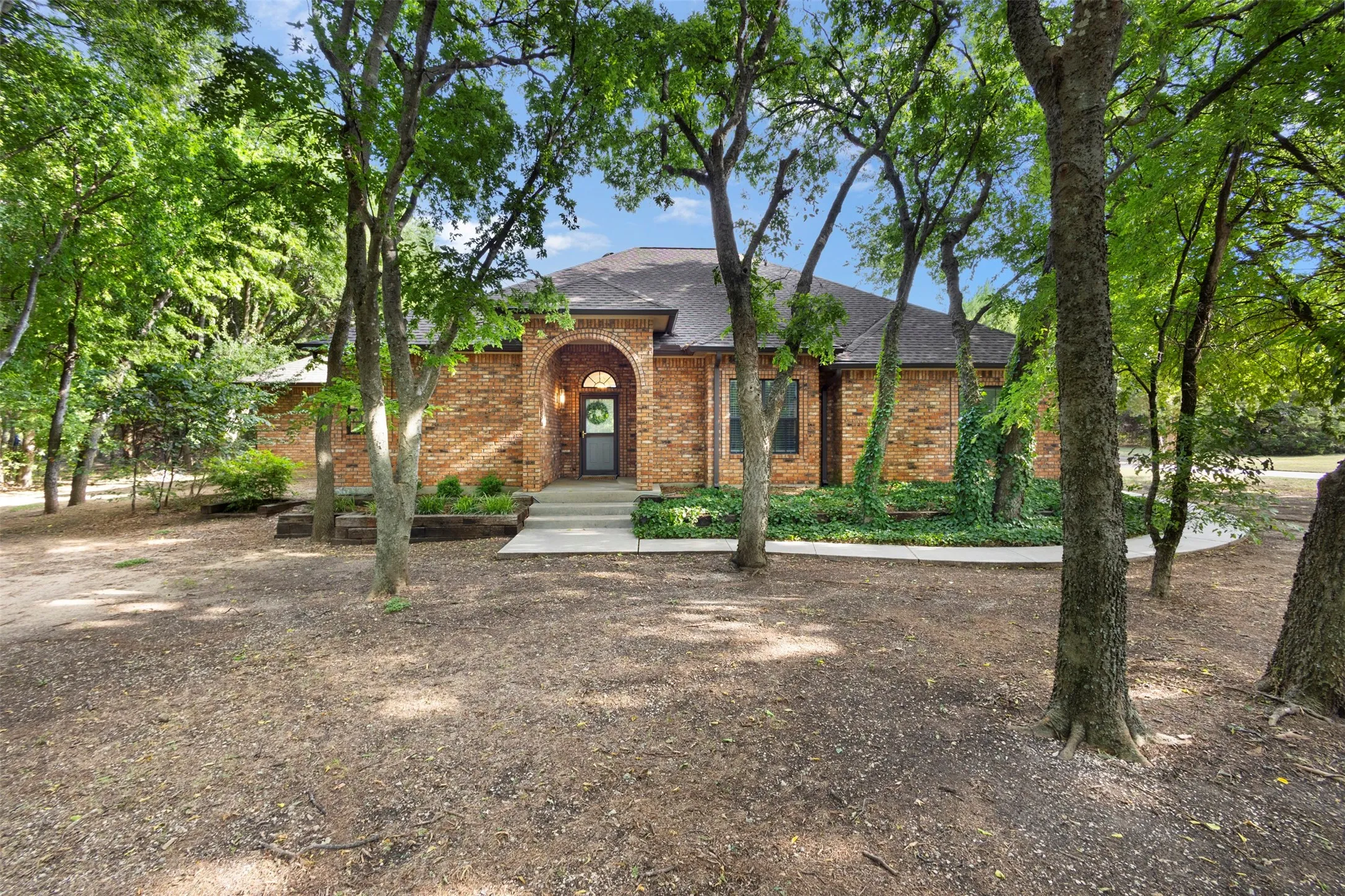 Brick exterior with arched entry, covered front porch, and established landscaping