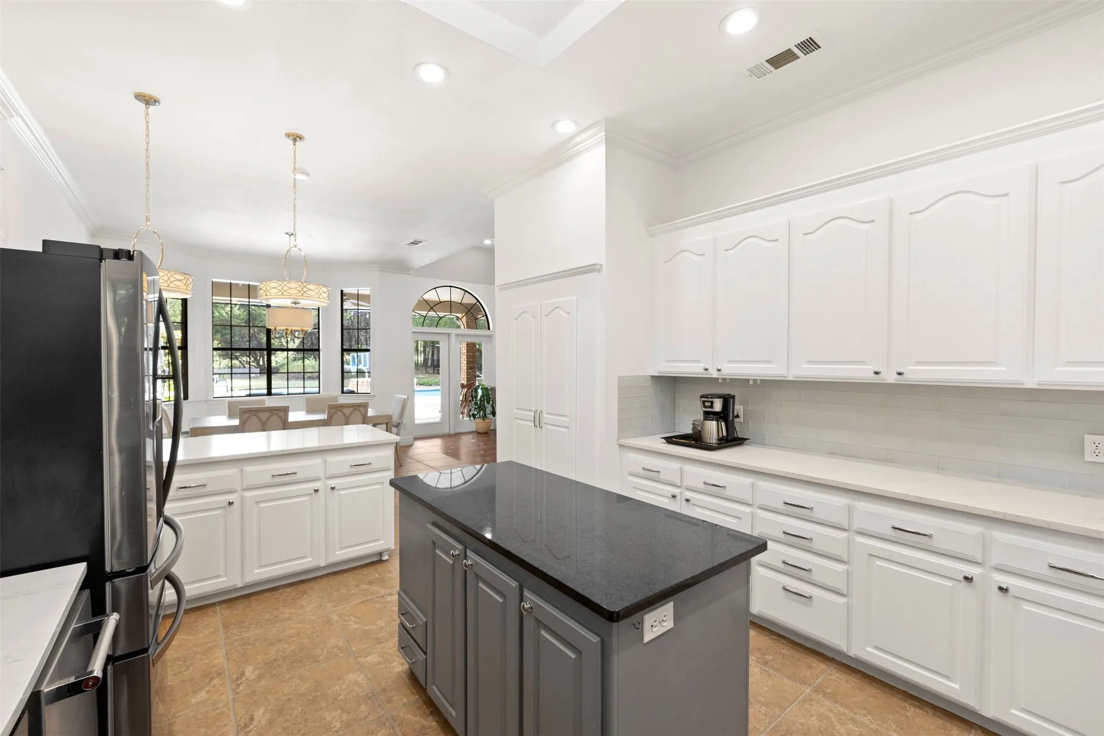 Spacious kitchen featuring white cabinetry, a large gray island with a dark countertop, stainless steel appliances, and tile flooring