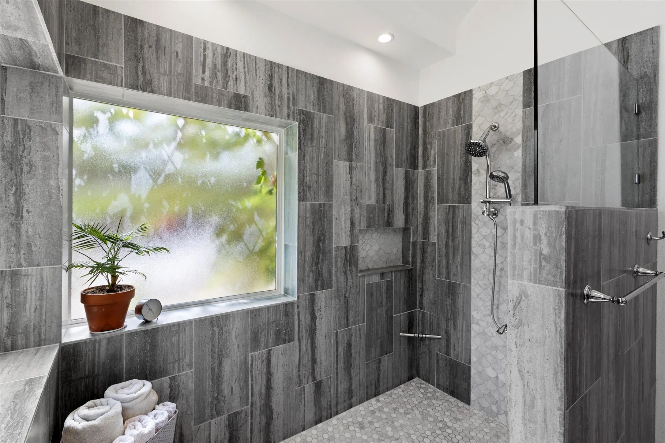 Walk-in shower featuring a built-in bench, glass enclosure, tiled walls, a shower niche, and pebble flooring