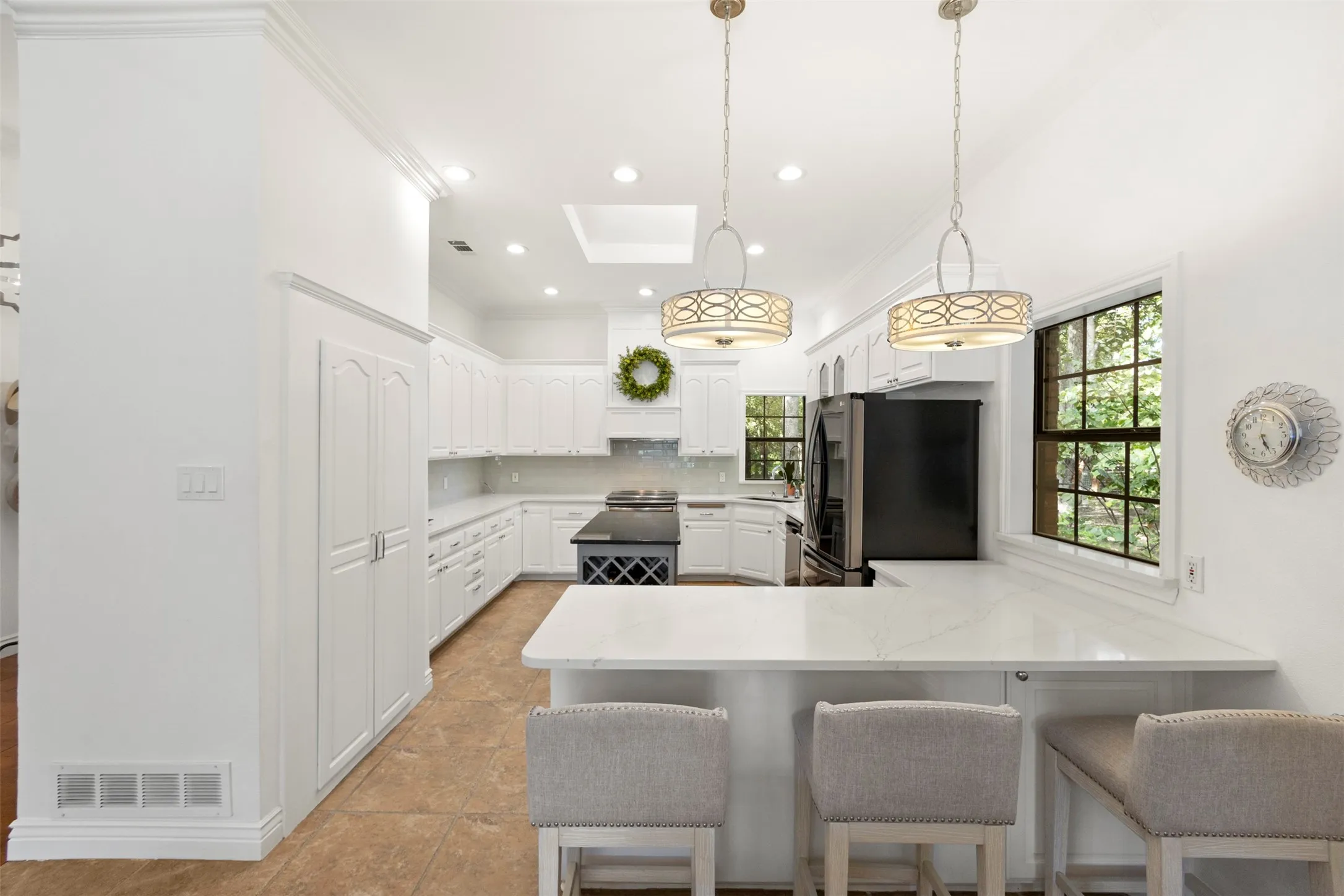 White cabinetry, white countertops, built-in pantry, central island with wine storage, and pendant lighting