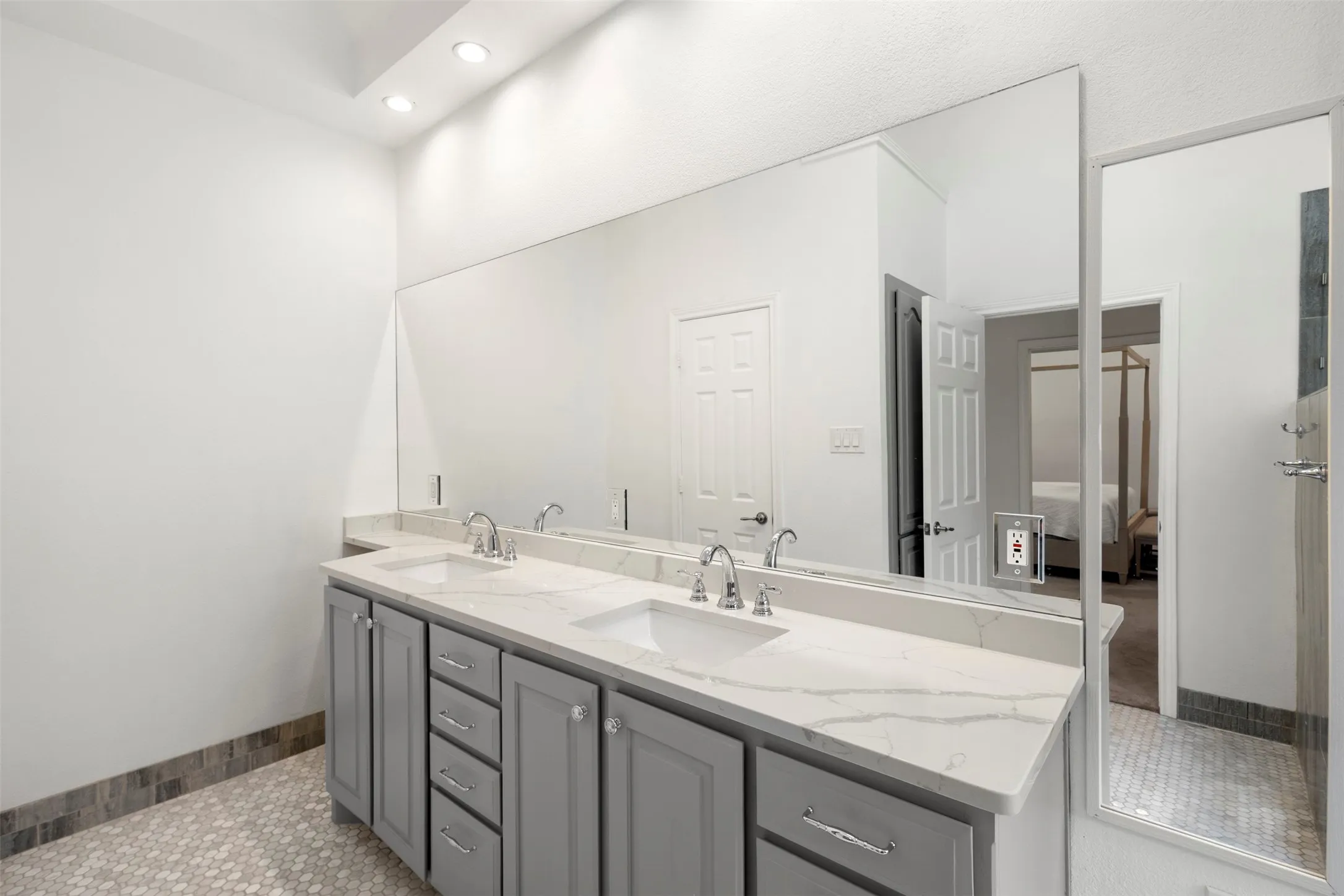 Dual vanity with integrated sinks, a continuous mirror, recessed lighting, and a hexagon tile floor
