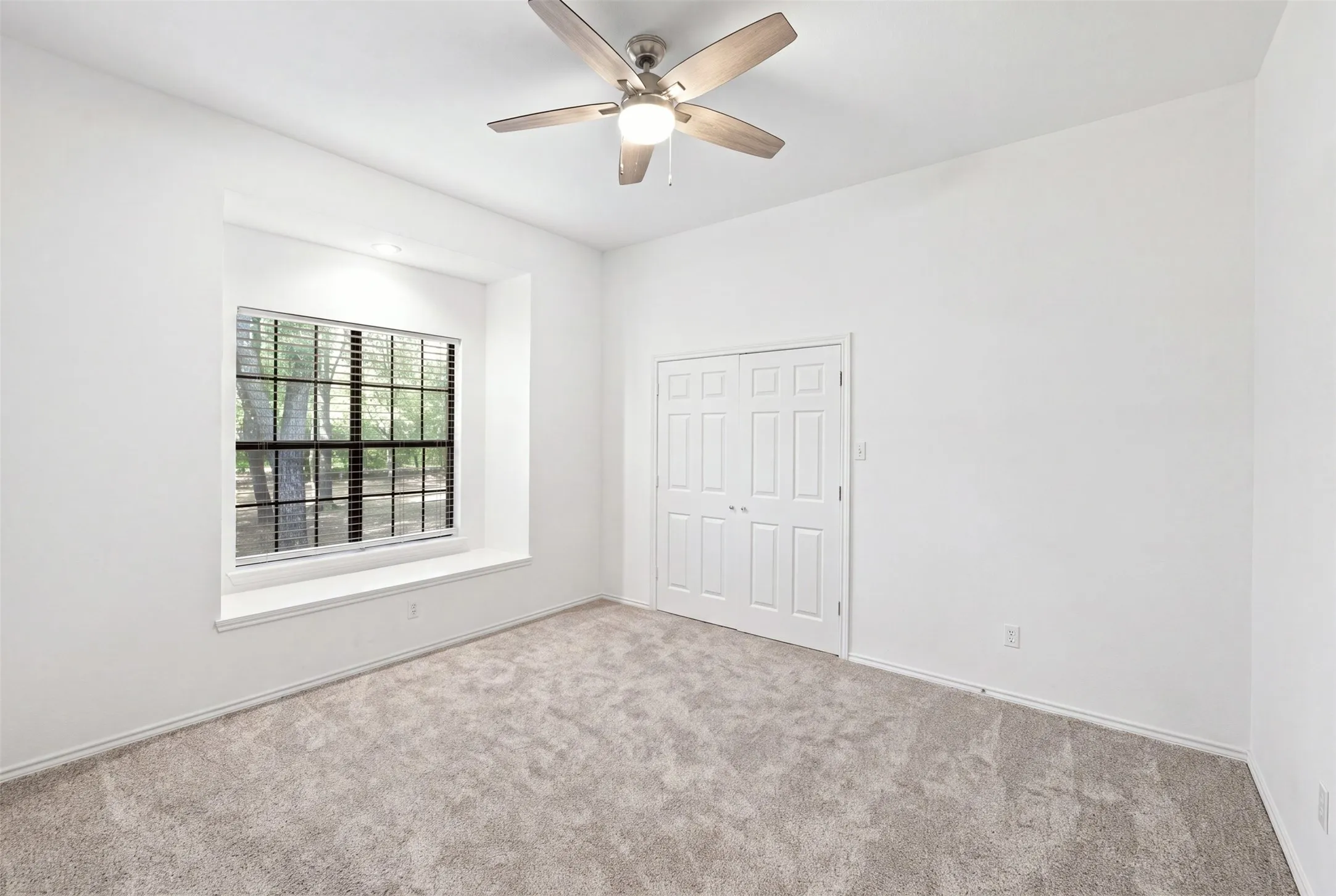 Recessed window with a deep sill, neutral carpeting, crisp white walls, ceiling fan, and double-door closet
