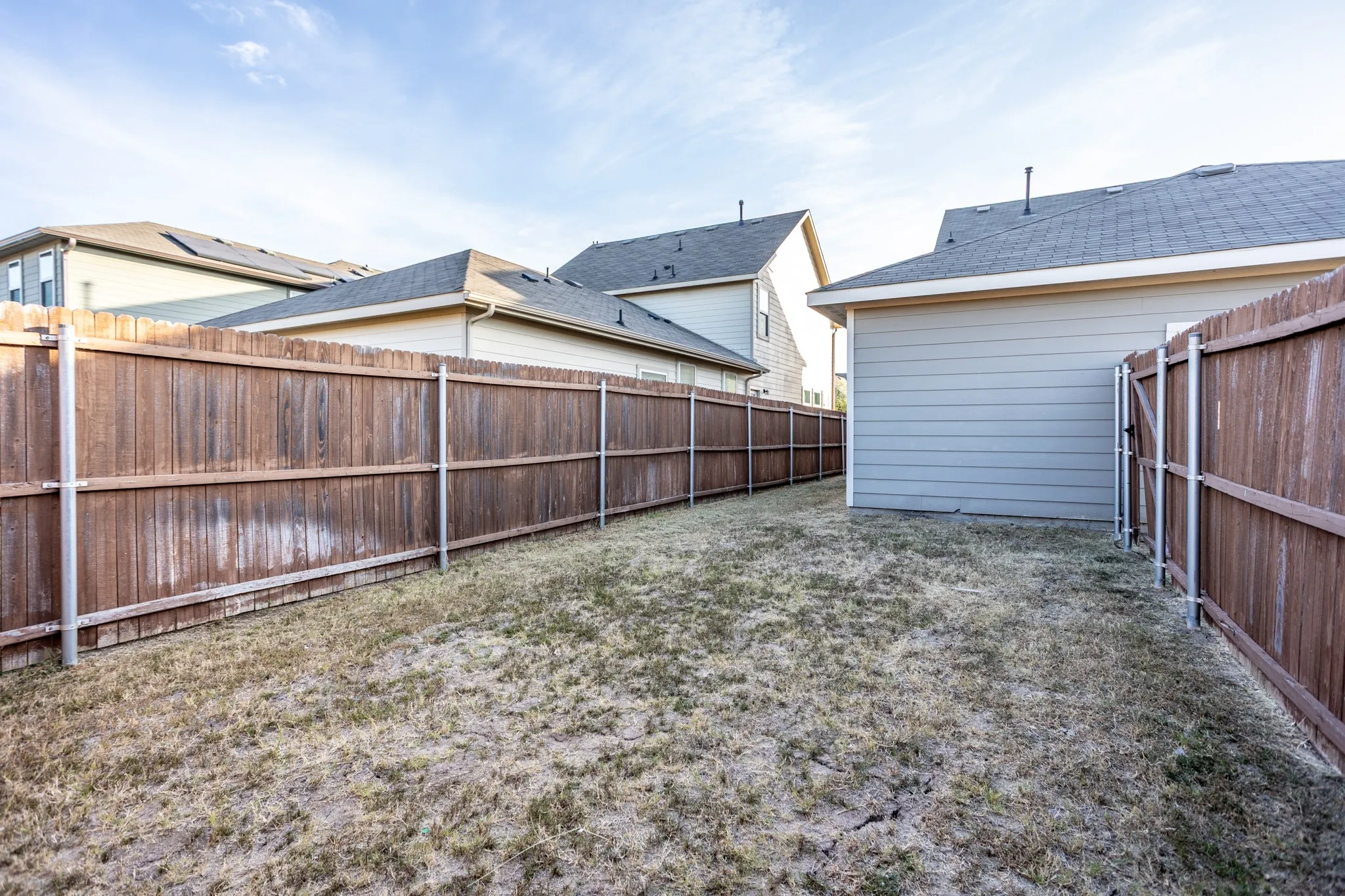 Private backyard area featuring wood fencing, a dedicated service gate, and horizontal siding on the rear of the structure