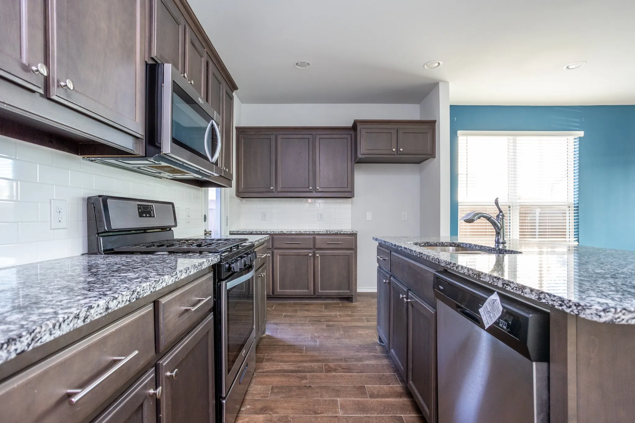 Kitchen featuring dark wood-finish cabinetry, stainless steel appliances, granite countertops, and white subway tile backsplash