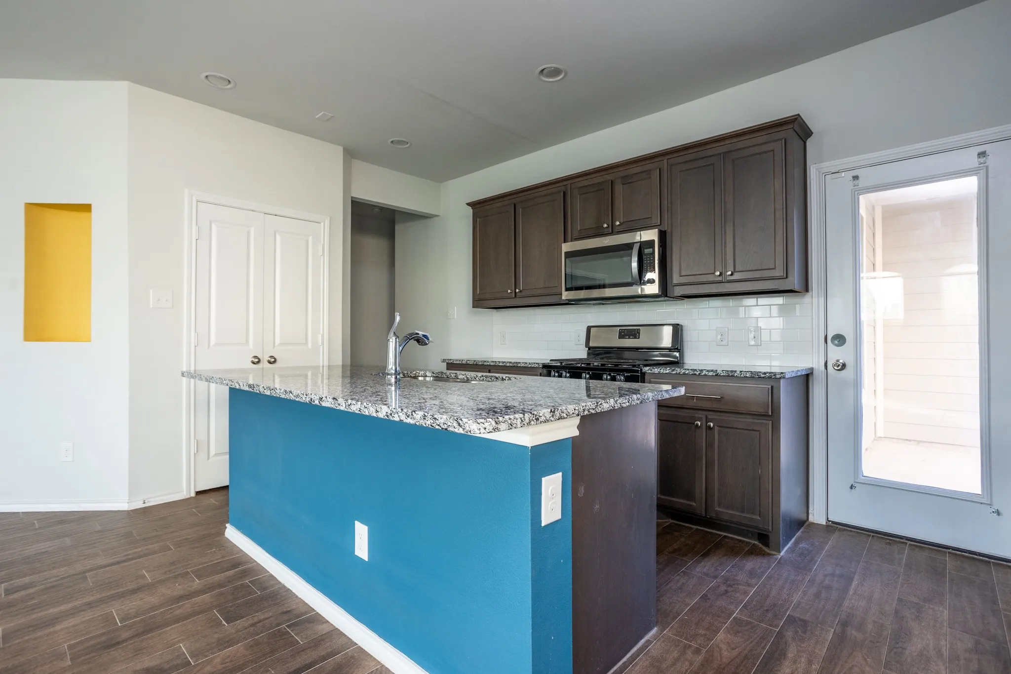 Kitchen featuring a central island with a granite countertop, stainless steel appliances, dark wood-finish cabinetry, subway tile backsplash, and wood-finish flooring