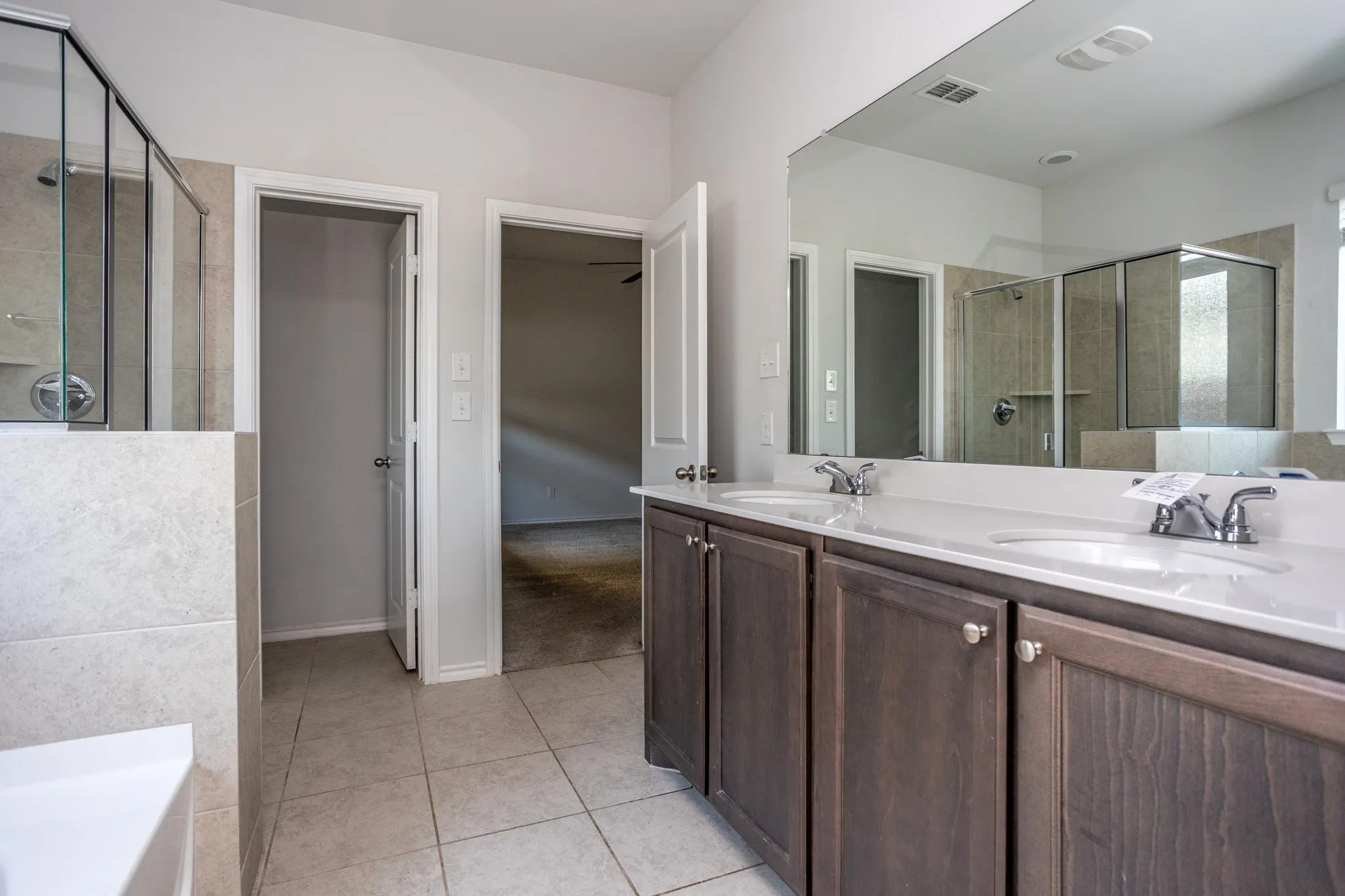 Spa-inspired primary bathroom featuring dual vanities with wood-finish cabinetry, white quartz countertops, and polished chrome faucetry