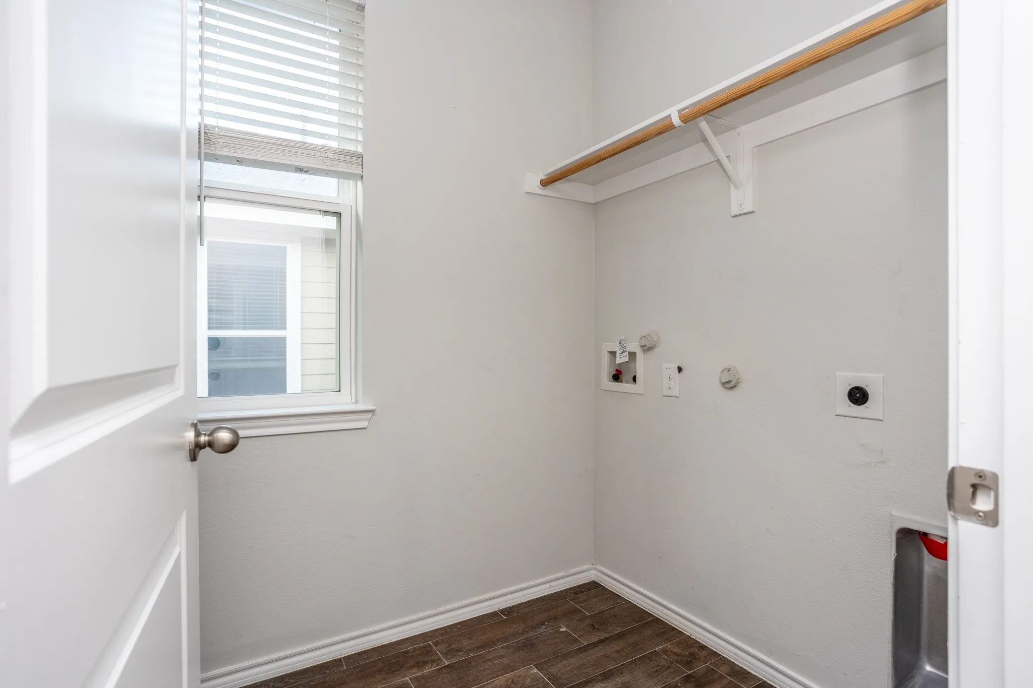 Utility area with wood-finish flooring, a window featuring blinds, a built-in hanging rod, and utility hookups