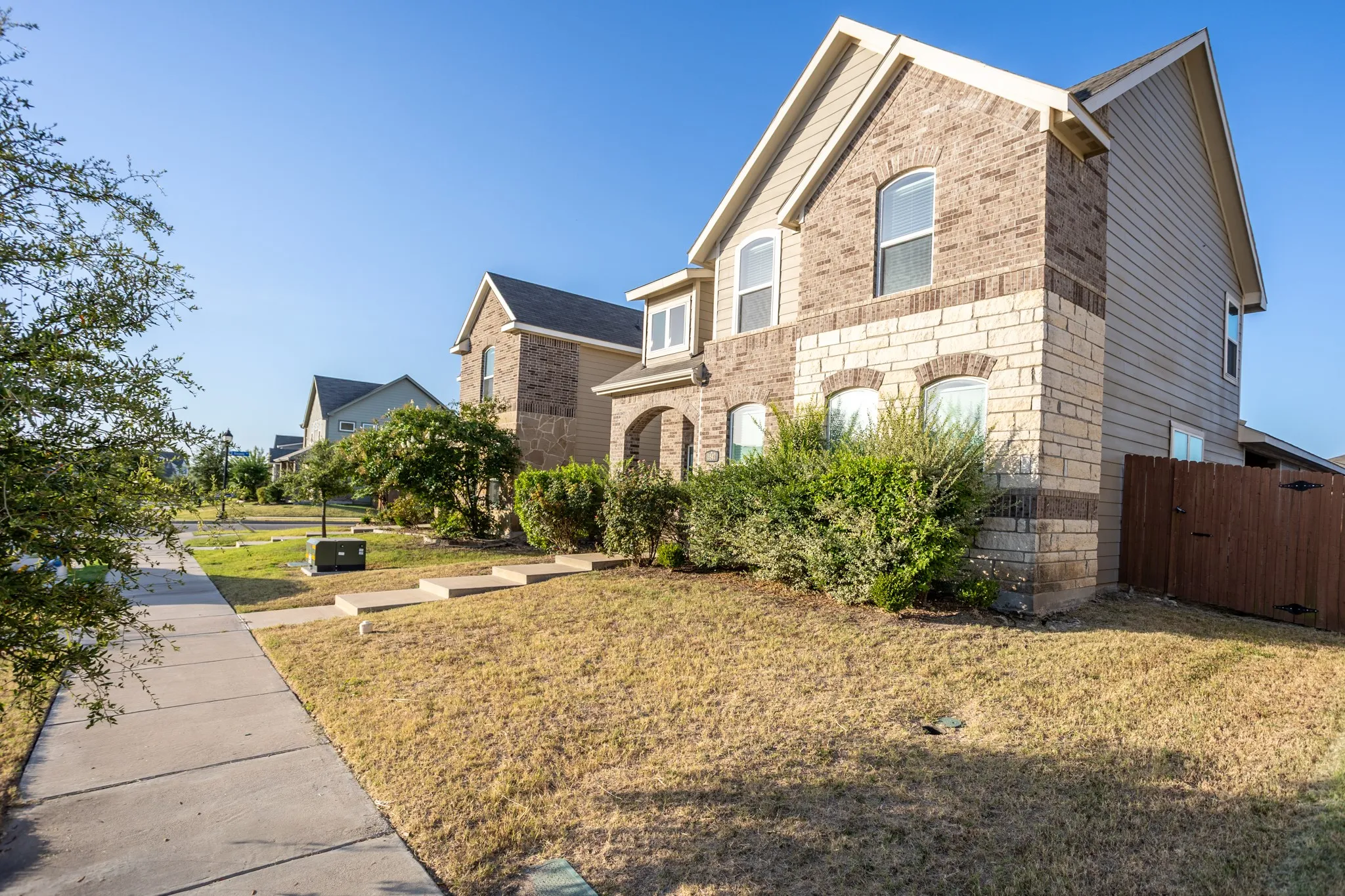 Two-story exterior featuring a brick and stone facade, arched windows, and a fenced side yard