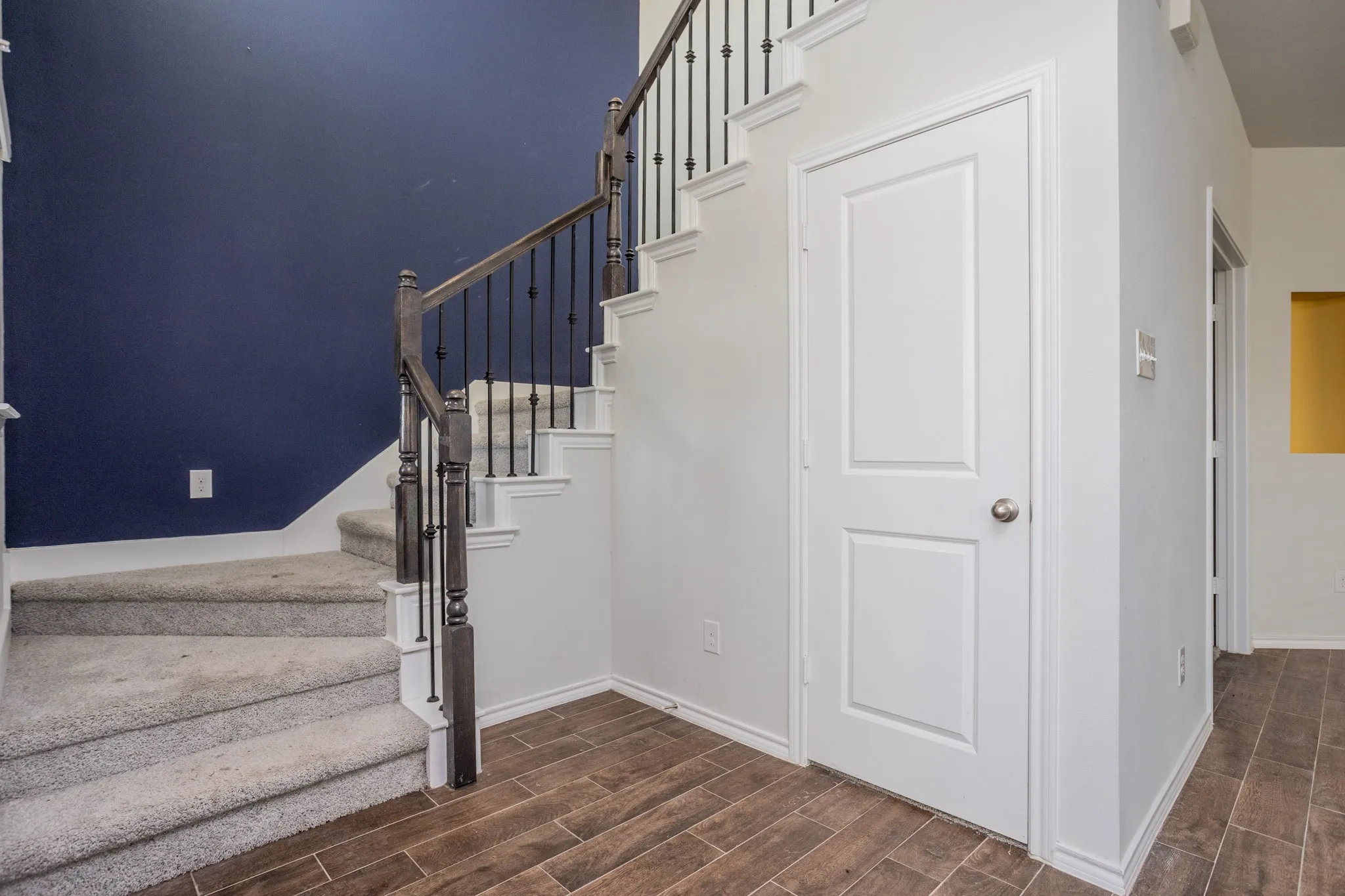 Modern foyer featuring a striking navy accent wall, wood-finish flooring, and a geometric staircase with metal railings