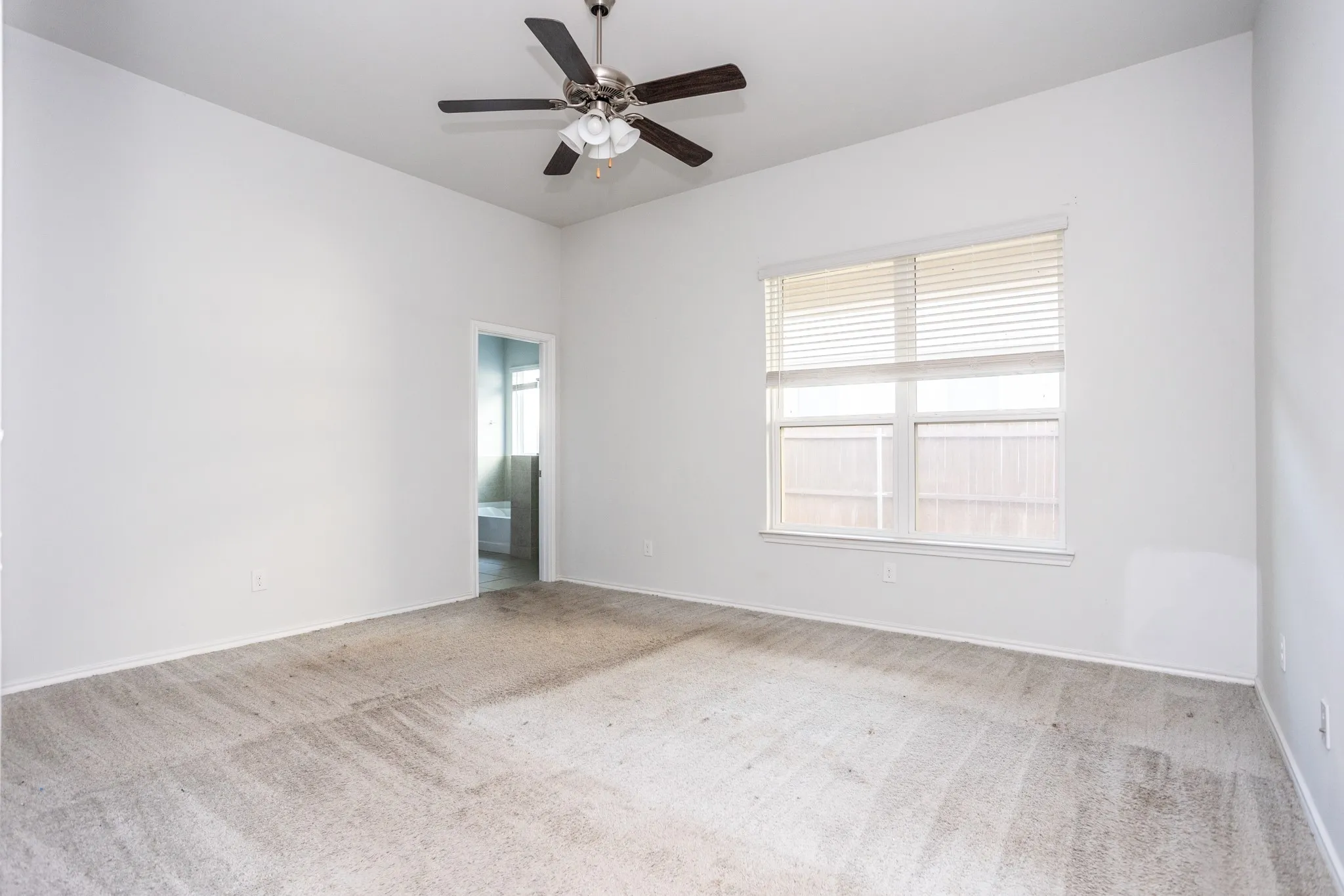 Spacious room with light neutral wall tones, a ceiling fan with integrated lighting, a large window with blinds, and neutral-toned carpeting