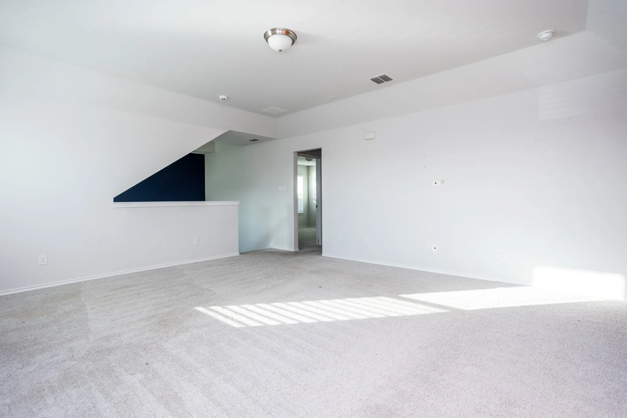Spacious carpeted room featuring white walls and a contemporary ceiling light fixture