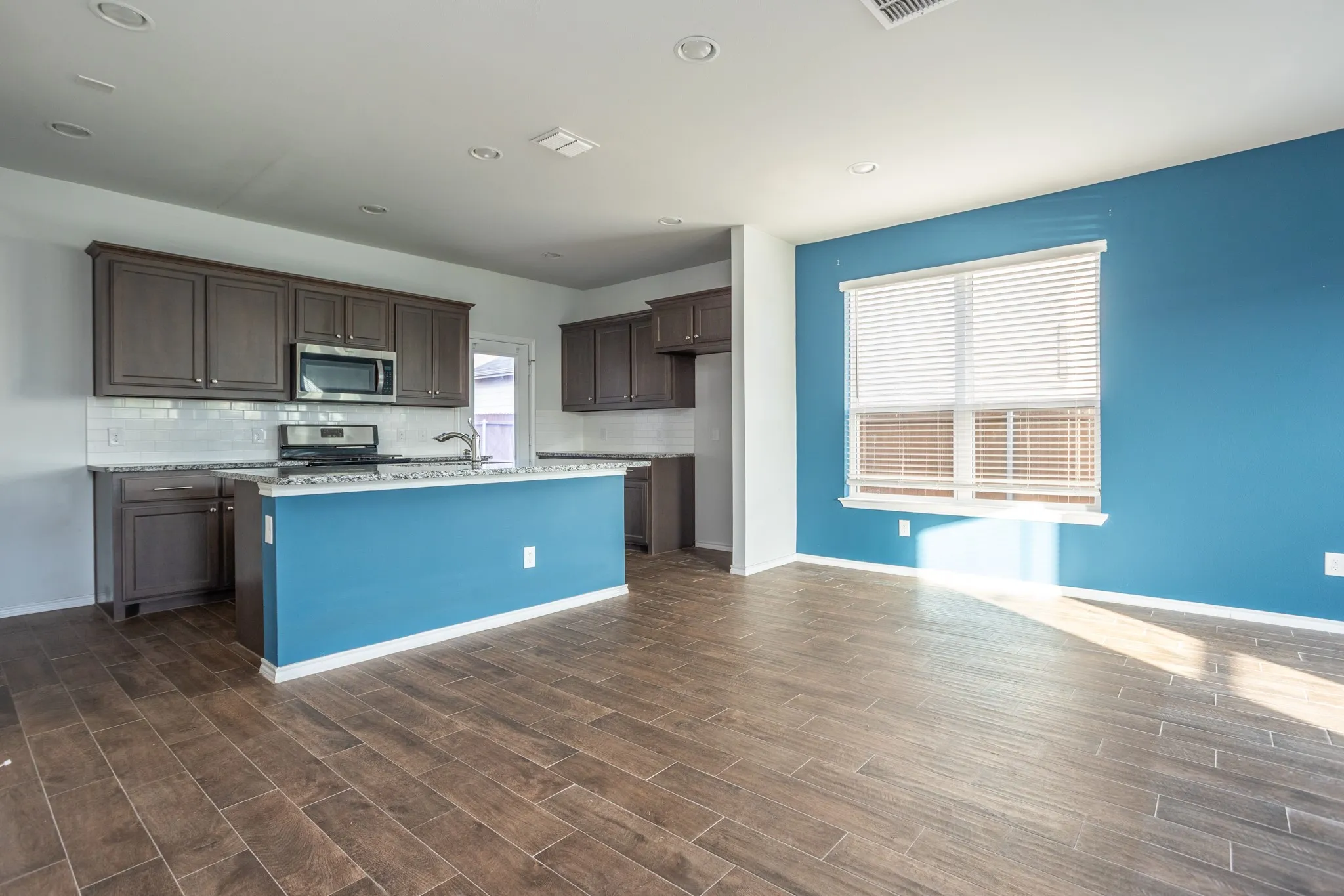 Open-concept living space with wood-finish tile flooring, recessed lighting, and a kitchen island with stone countertops