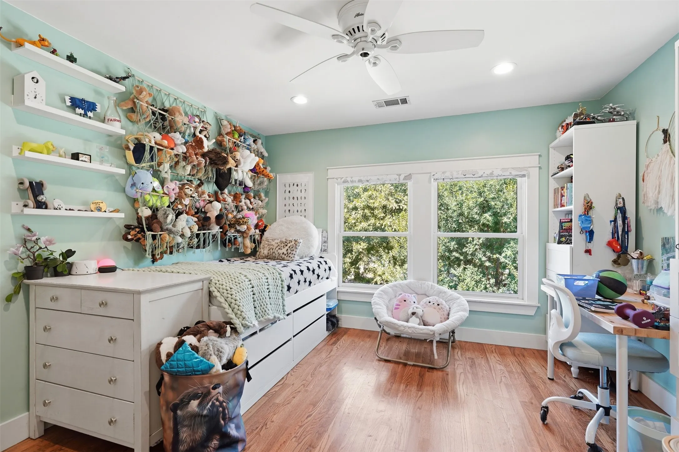 Hardwood-finish flooring, dual windows with exterior tree scenery, ceiling fan, recessed lighting, and wall-mounted shelving
