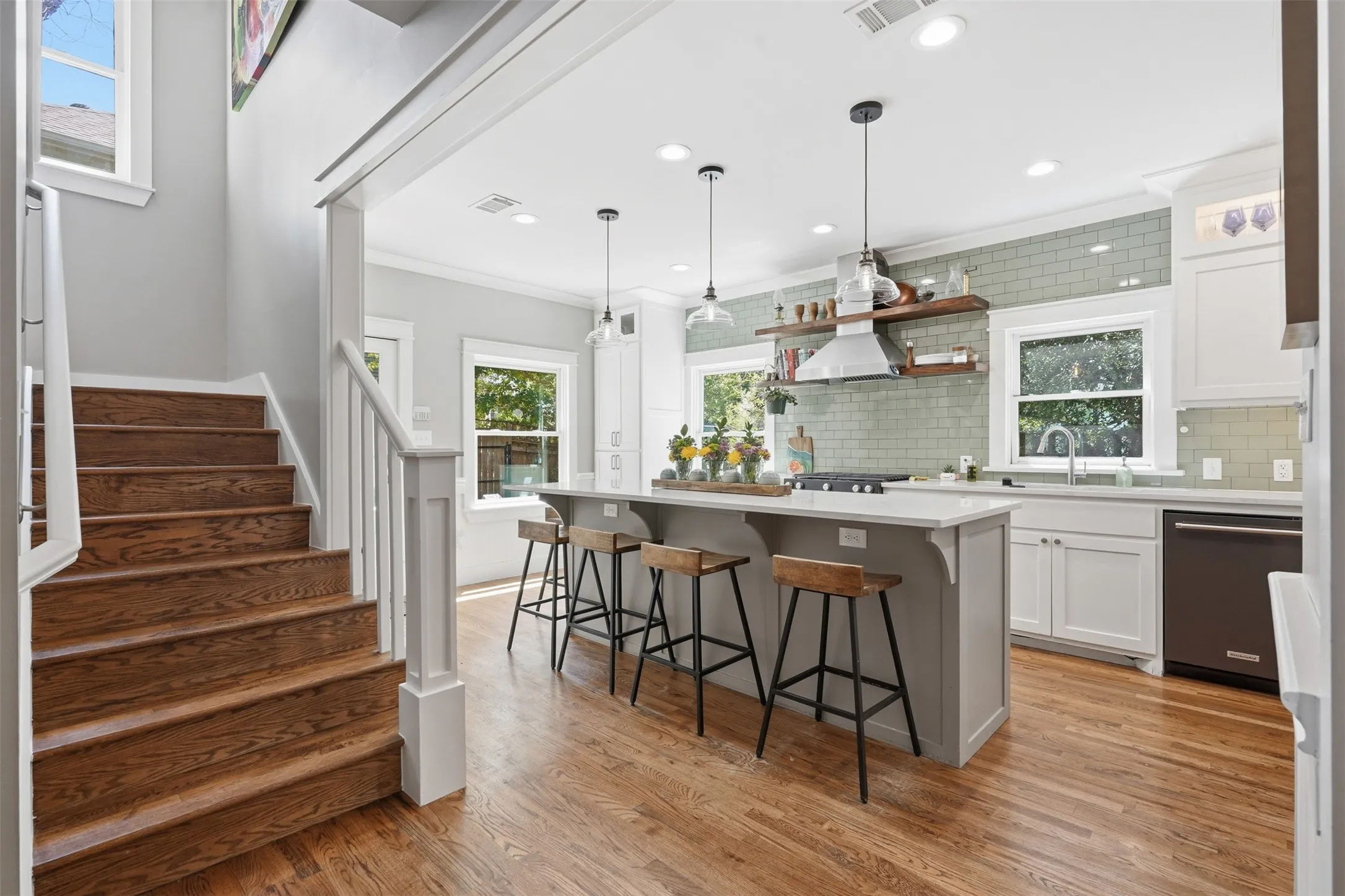 Hardwood flooring throughout, a kitchen island with seating, a subway tile backsplash, white cabinetry, and stainless steel appliances