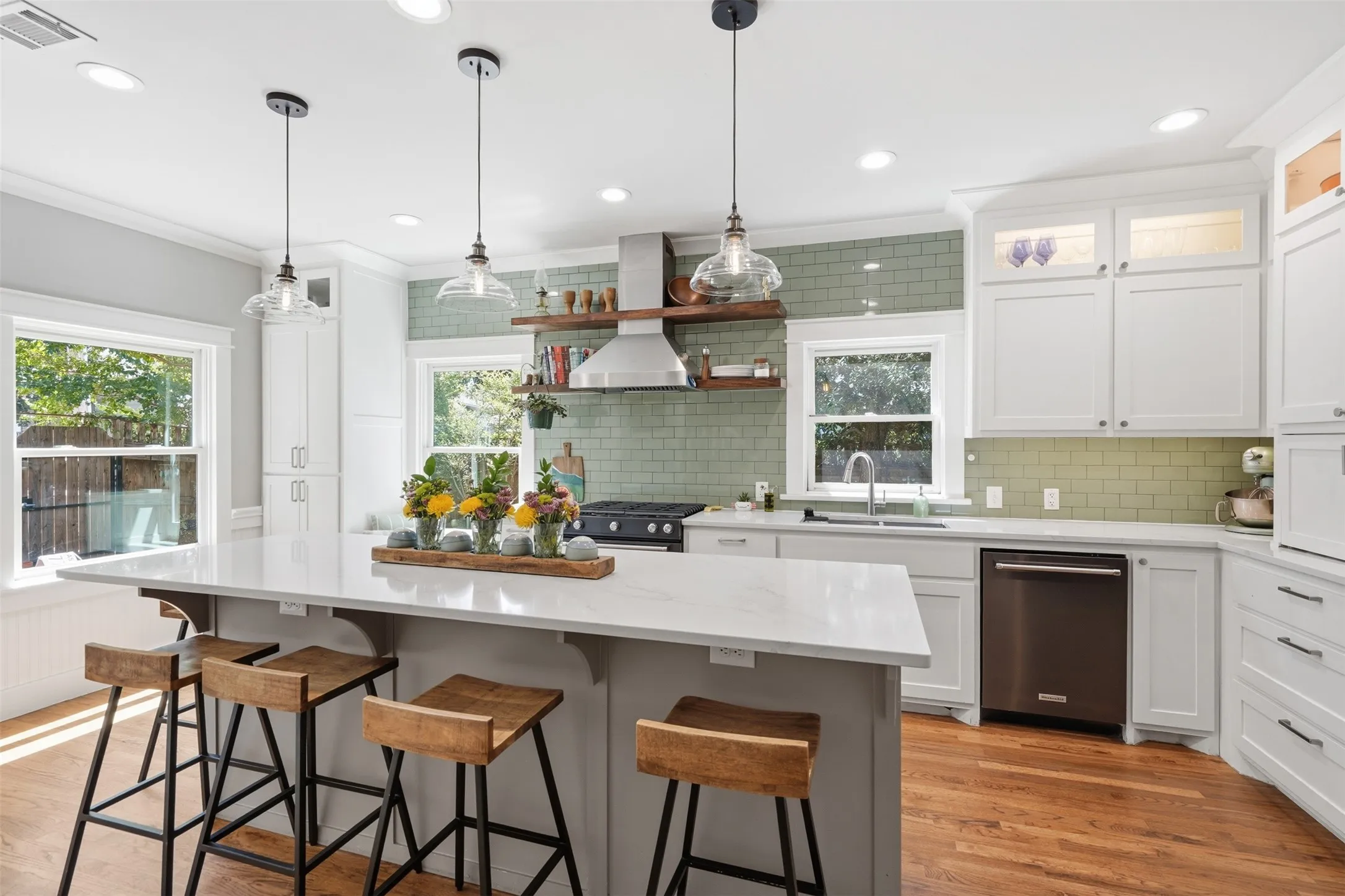 Kitchen featuring a large island with seating, white shaker cabinetry, light-toned countertops, a full stainless steel appliance package, and wood-finish flooring
