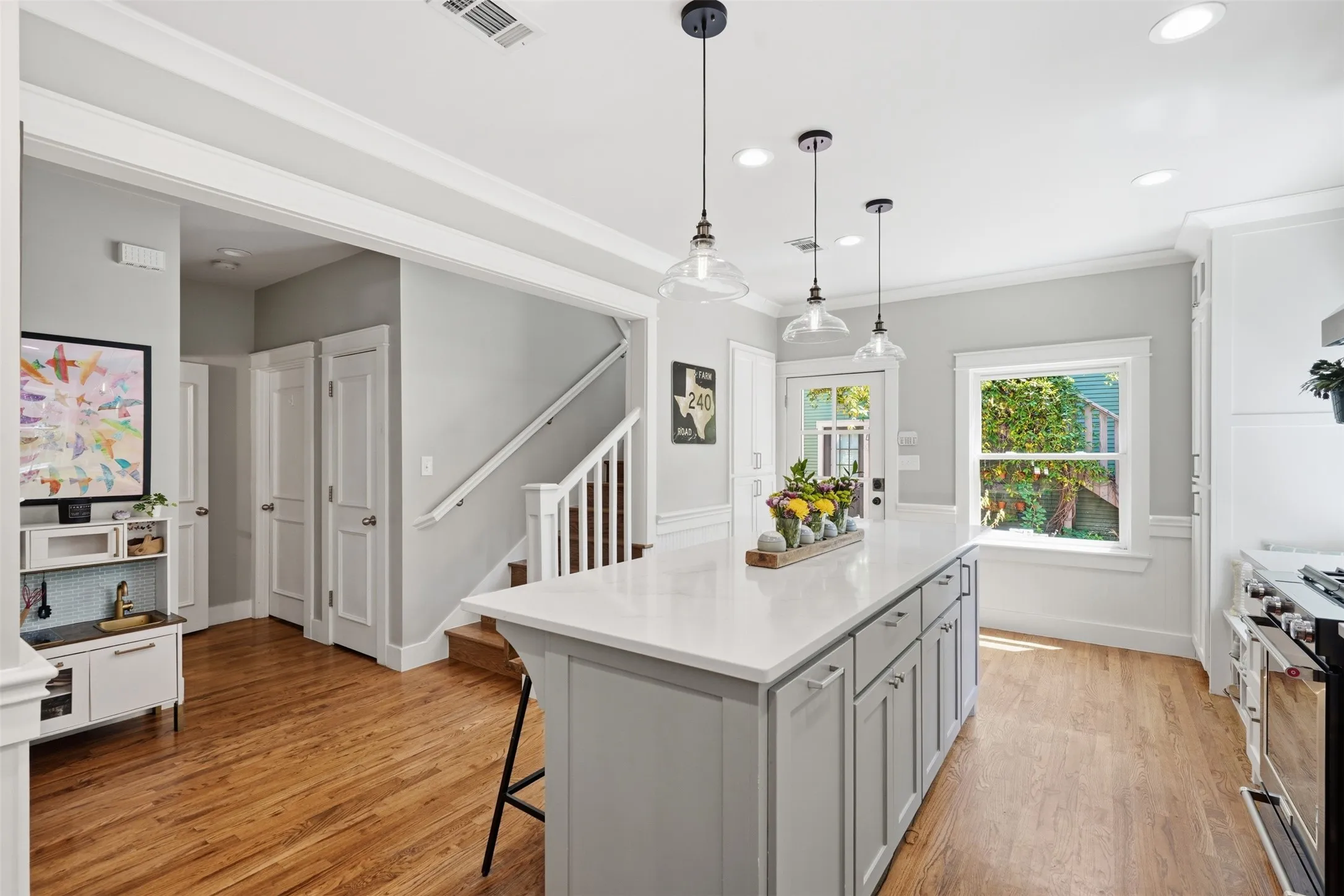 Kitchen island with a light-toned countertop, pendant lighting, wood-finish flooring, white cabinetry, and a double-pane window