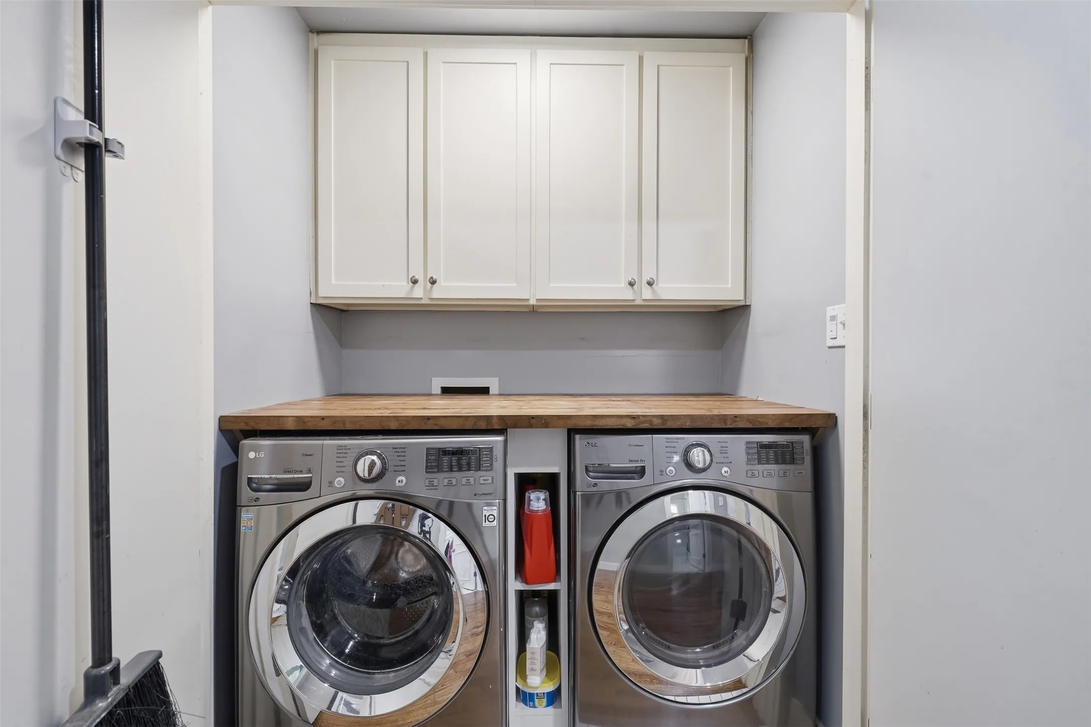 Integrated laundry area featuring wood-finish countertop, built-in open shelving, and upper cabinetry