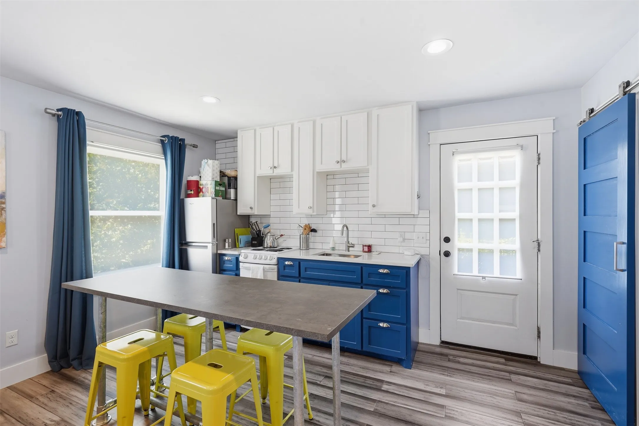 Kitchen featuring two-tone cabinetry, white subway tile backsplash, stainless steel sink, and wood-finish flooring