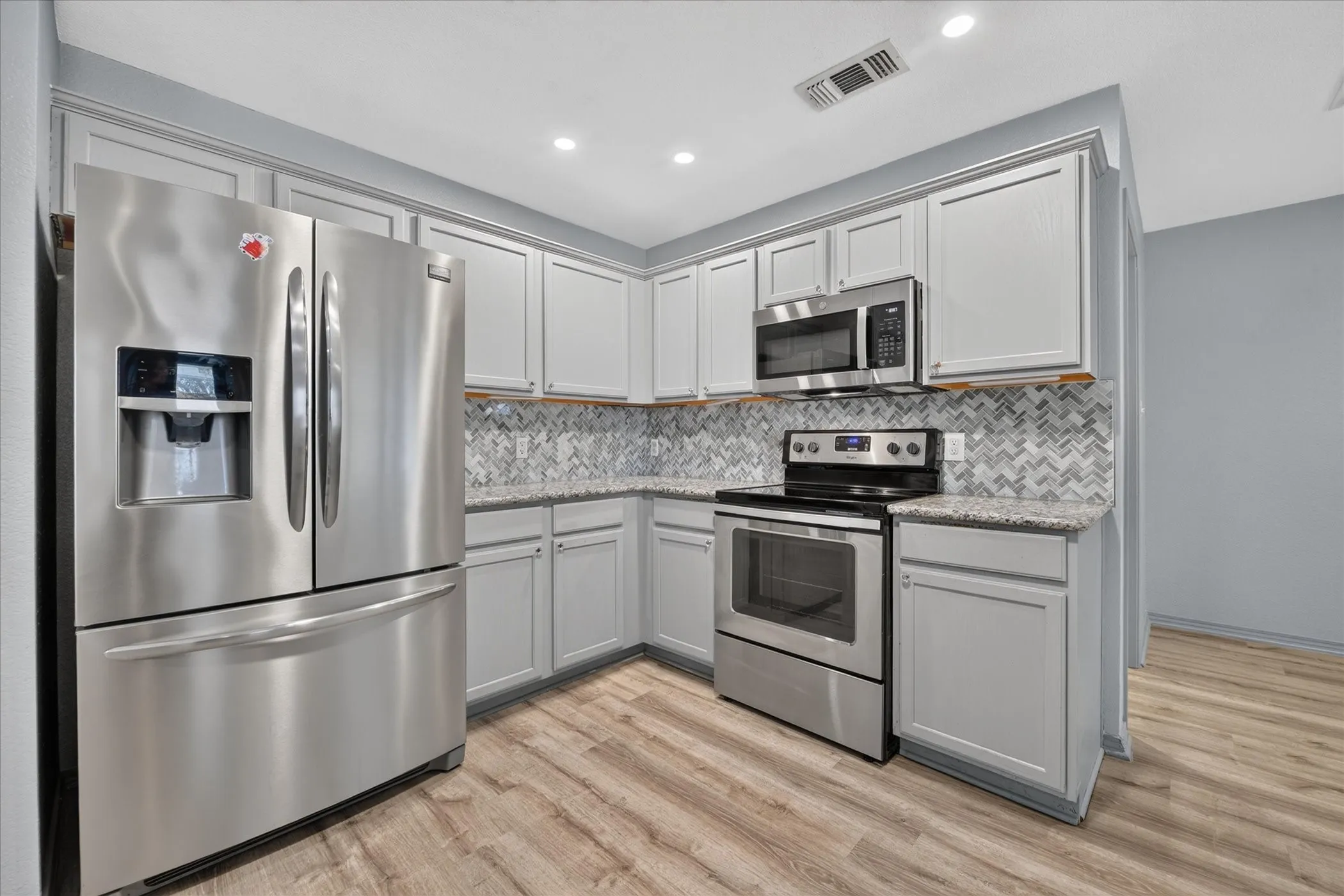 Modern kitchen featuring stainless steel appliances, light gray cabinetry, a herringbone tile backsplash, and wood-finish flooring