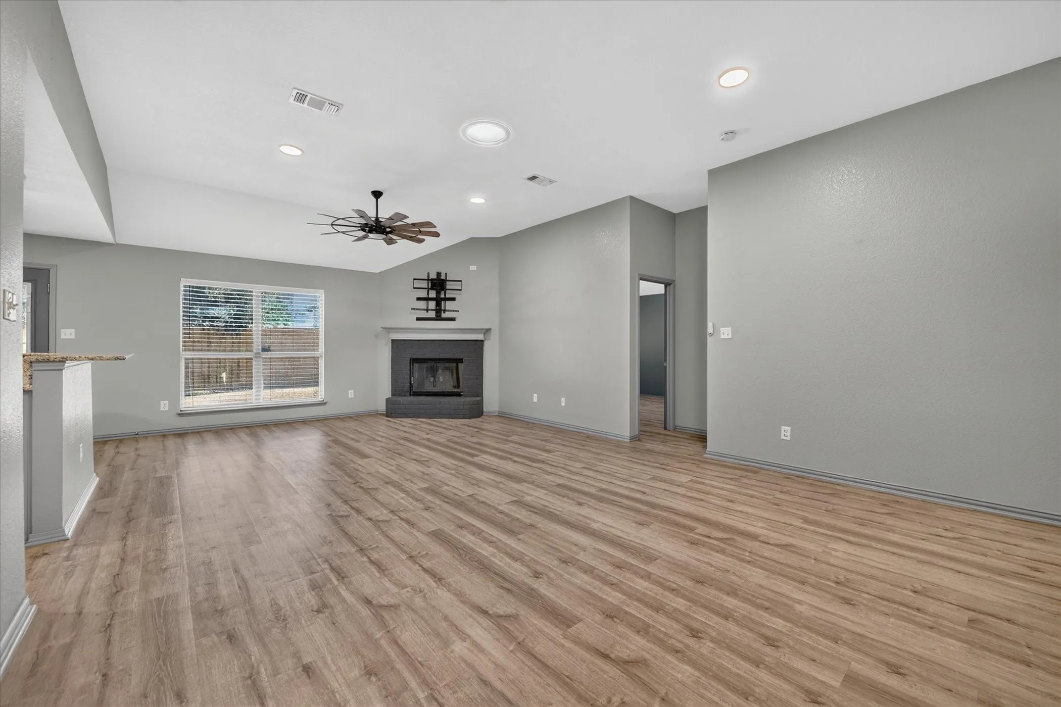 Wood-finish flooring, vaulted ceiling, recessed lighting, ceiling fan, and a fireplace with a mantel